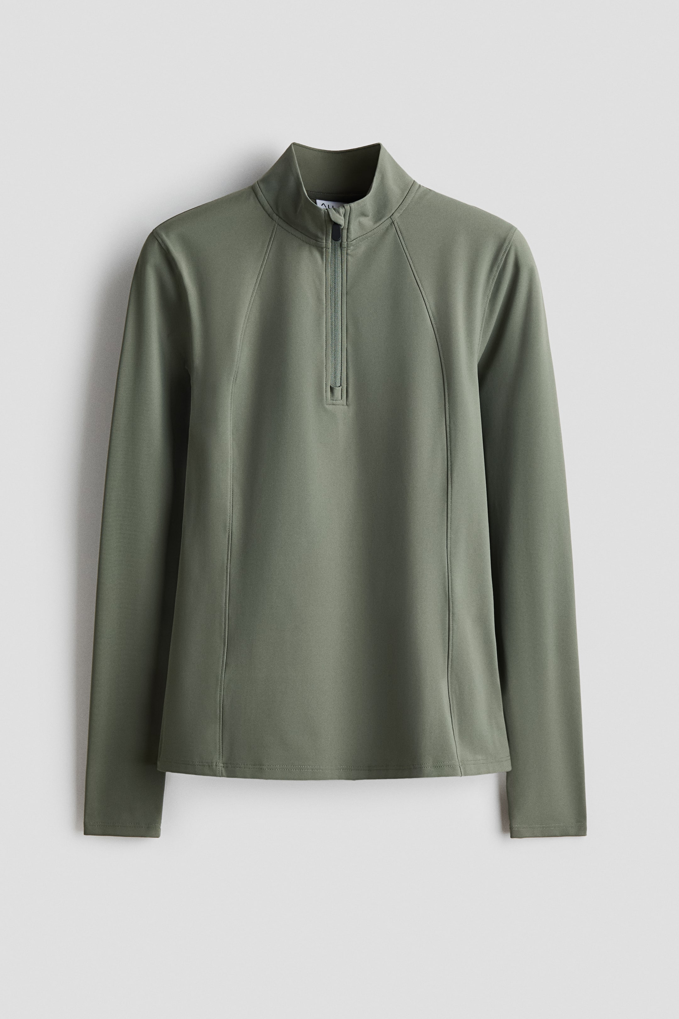 View larger image: A long-sleeved sports top in olive green is shown from the front. It is designed with a stand collar and a partial zip at the top, featuring an anti-chafe chin guard. Raglan seams are also visible across the front.