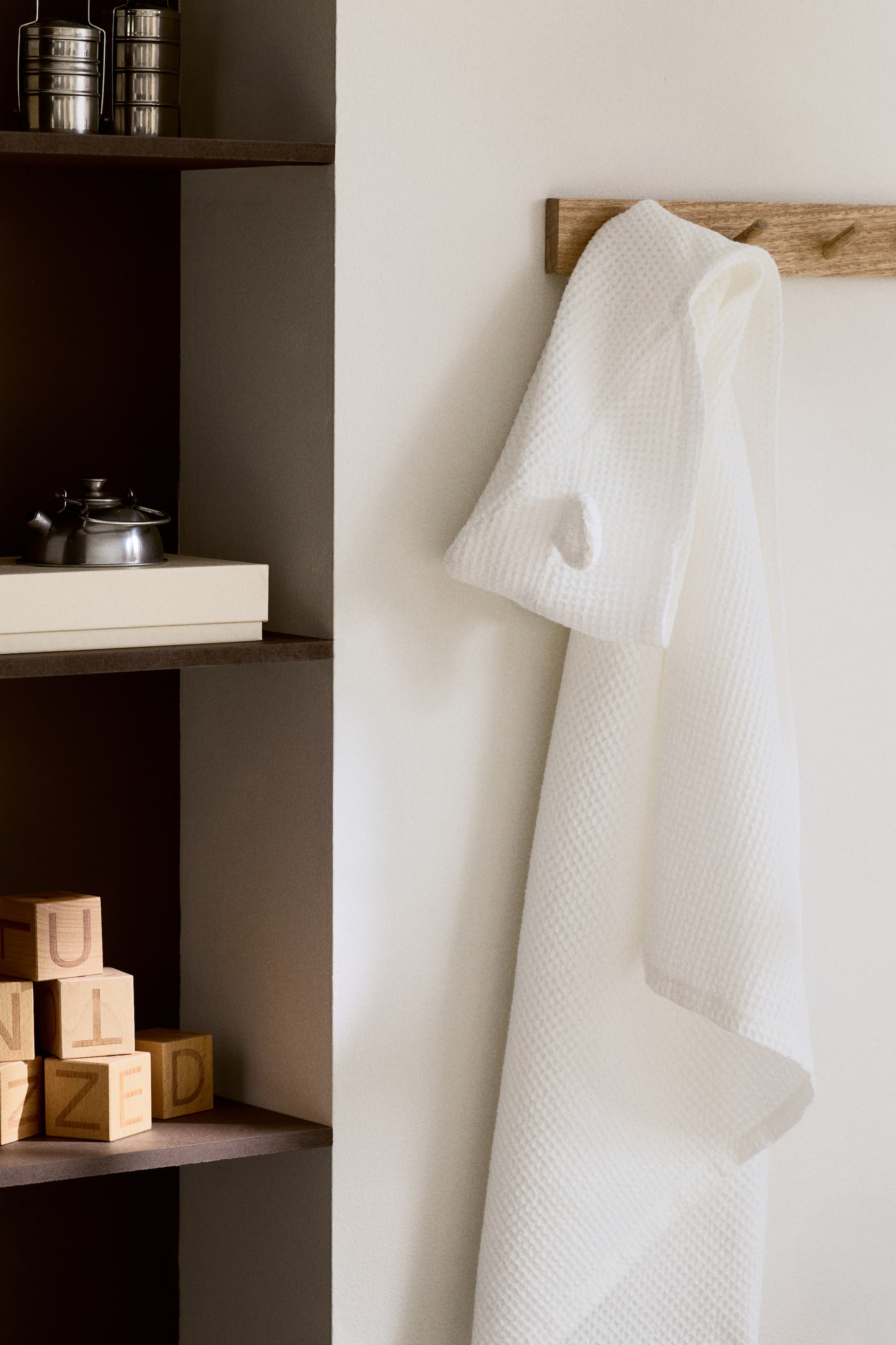 View larger image: Hooded bath towel. This white, waffle-weave towel is hanging from a wooden peg hook. The hood is visible at the top, featuring a small, rounded protrusion on one side.