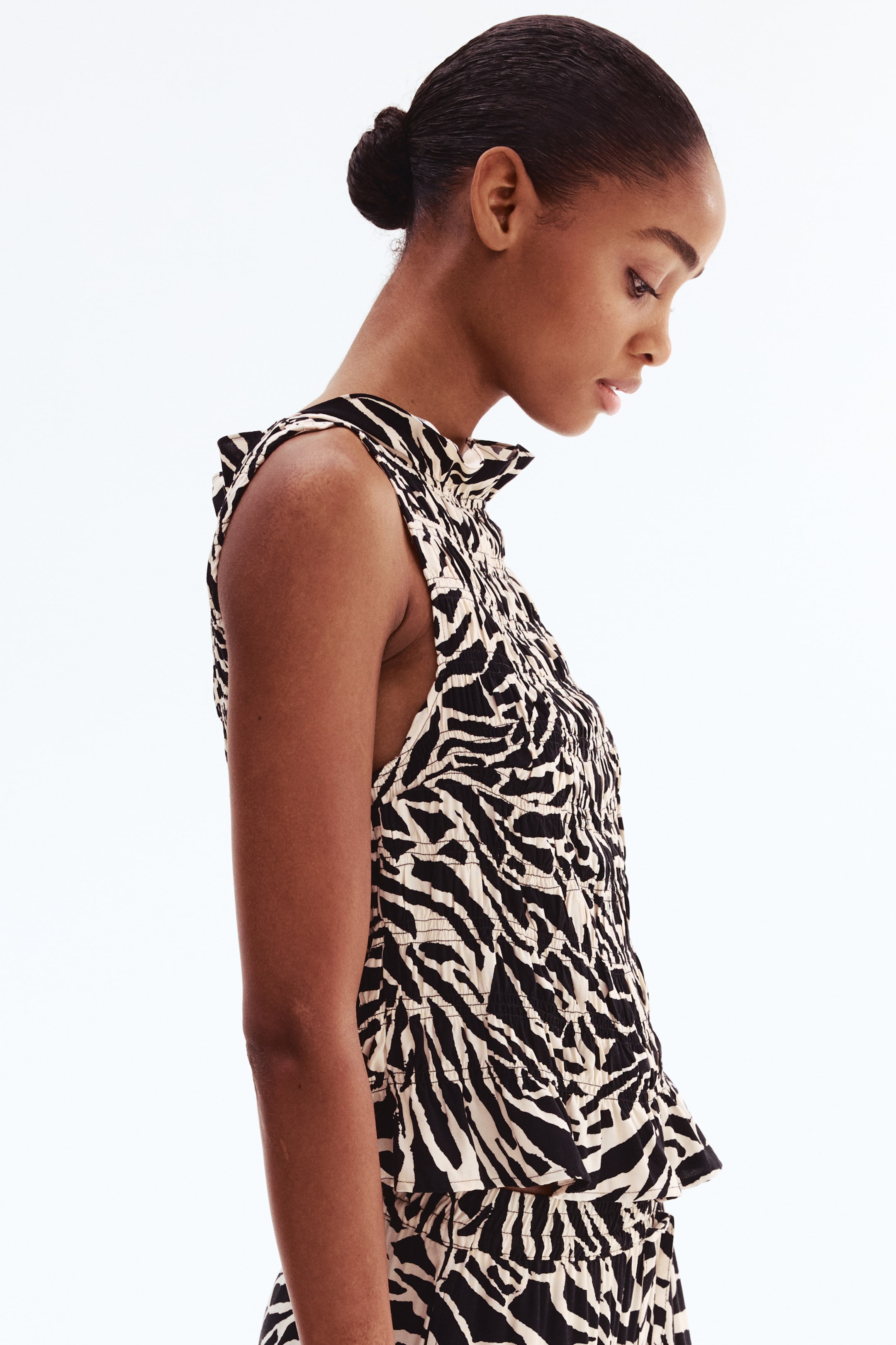 View larger image: A fitted, sleeveless top in a smocked viscose weave with a black-and-beige animal print, a frill-trimmed boat neckline, and a frill-trimmed hem, worn by the model.