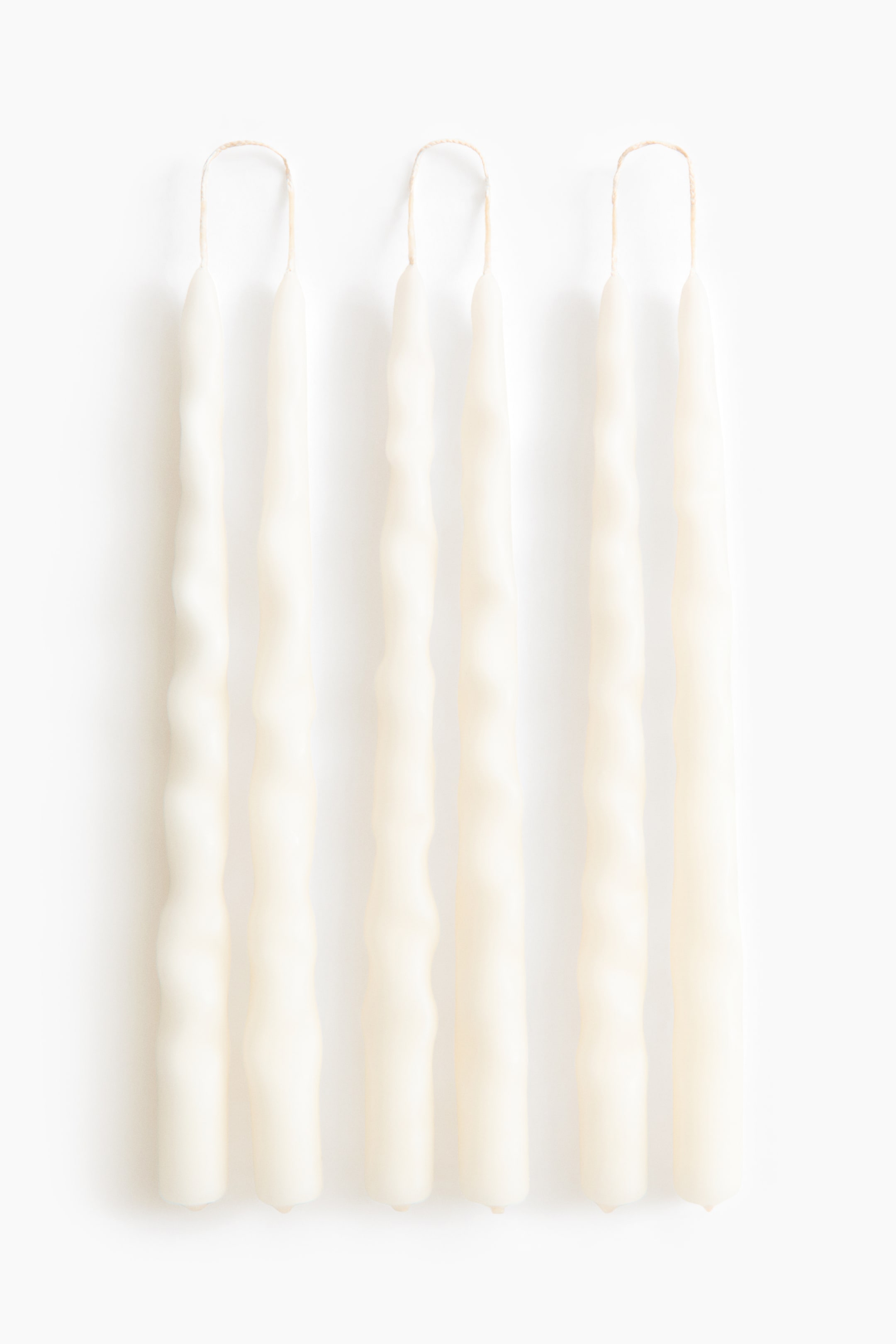 Grösseres Bild ansehen: Sechs elfenbeinfarbene, konische Kerzen sind von vorne zu sehen und präsentieren ihr unverwechselbares, handgeformtes Design mit welligen, unregelmässigen Oberflächen. Jede Kerze verfügt über einen geschlungenen Docht an der Spitze, und Kerzenpaare sind durch diese Dochte miteinander verbunden.