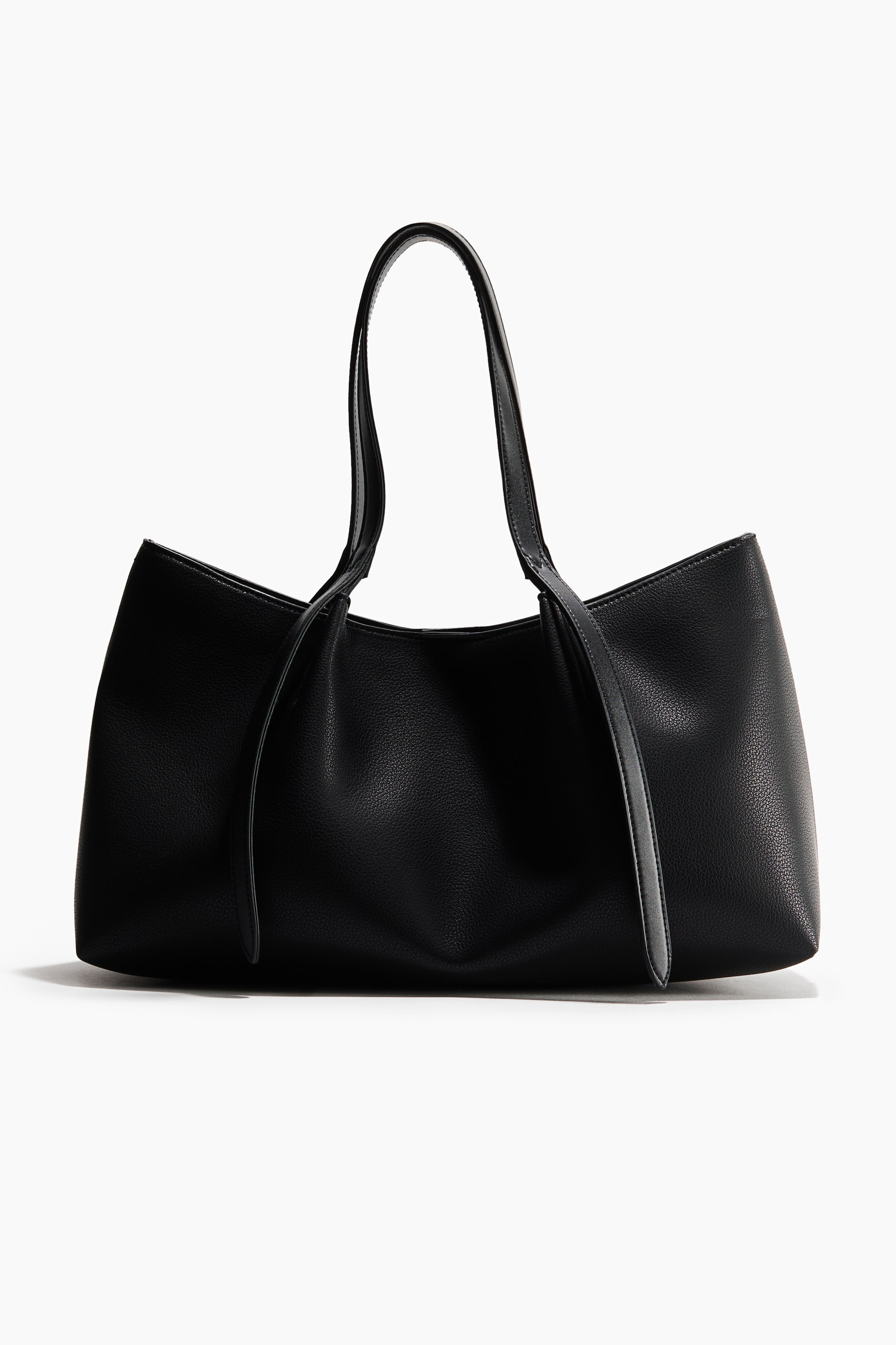 View larger image: A black pebbled leather tote bag is shown in a front-facing view, highlighting its soft, slouchy structure and textured finish. It features two slim top handles with long, flat strap ends draping down the front of the bag.