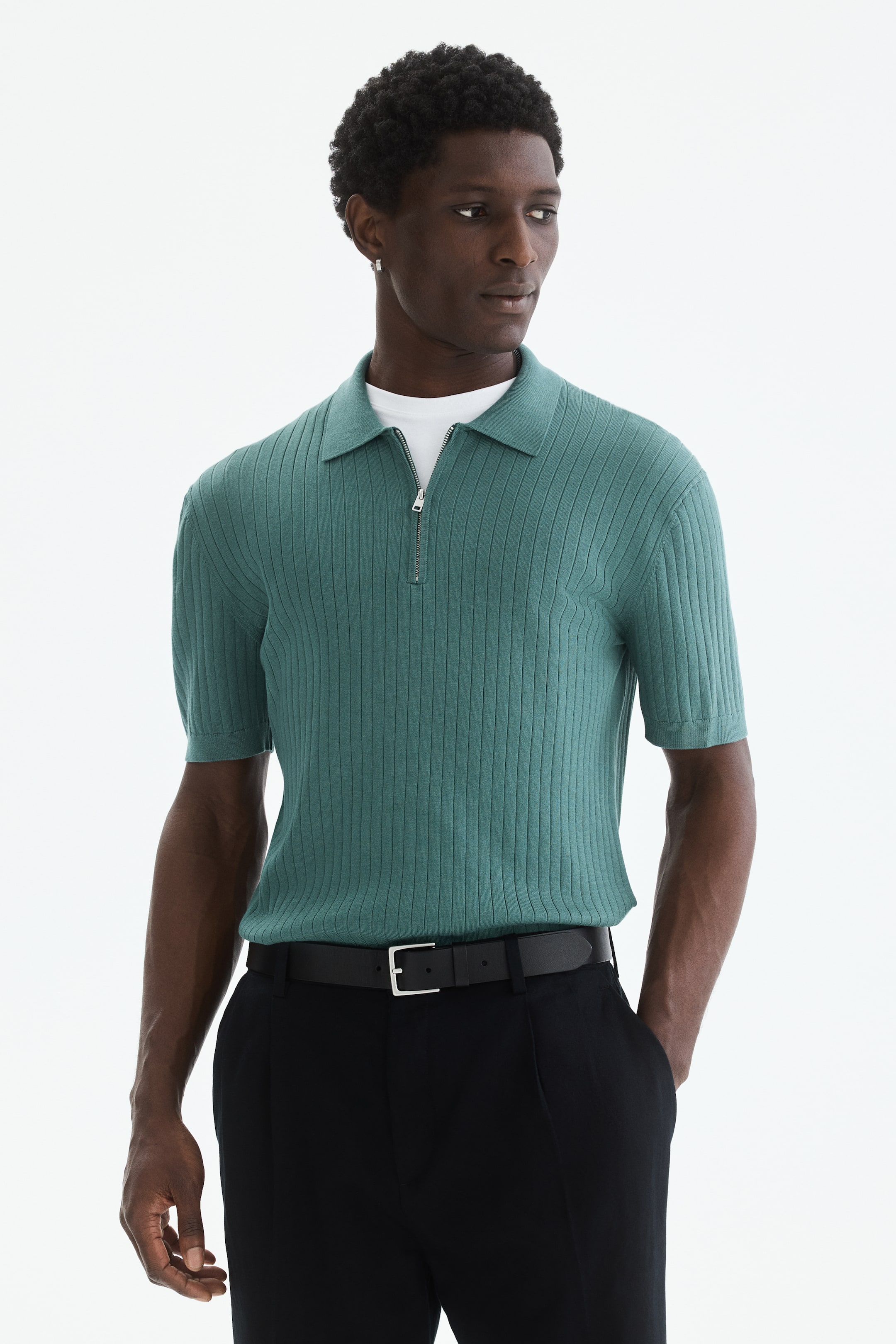 View larger image: Wearing a teal ribbed knit polo shirt with a pointed collar, a quarter-zip placket adorned with a silver zipper, short ribbed sleeves, and a ribbed hem, layered over a white t-shirt.