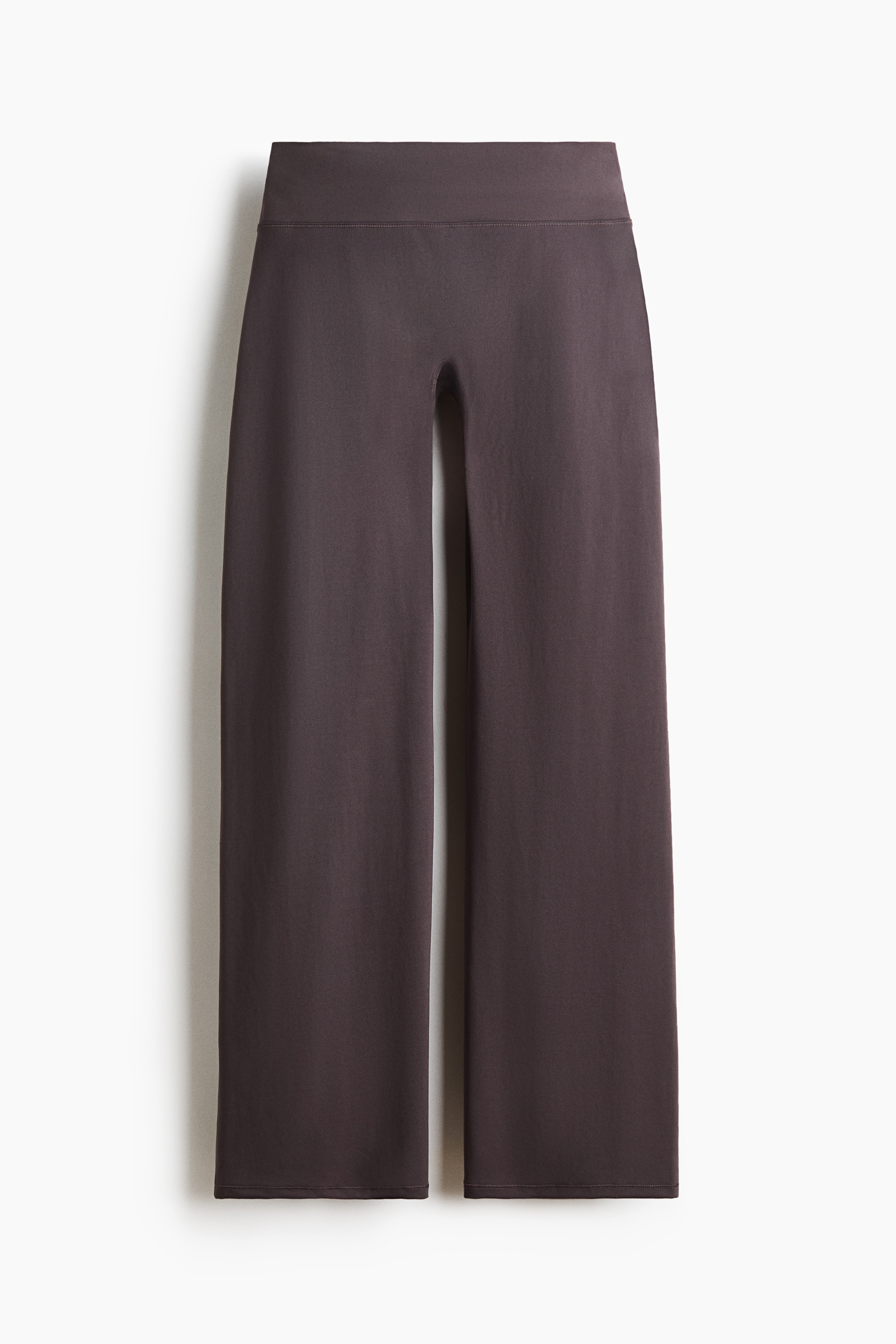 Een crÃ¨mekleurige wikkeltop met lange mouwen wordt gedragen door het model, gestyled over een bijpassende cropped top met ronde hals en gecombineerd met donkerbruine wide-leg broek. De wikkeltop heeft een diepe crossover-halslijn en lange mouwen, getoond terwijl het model in kleermakerszit zit.