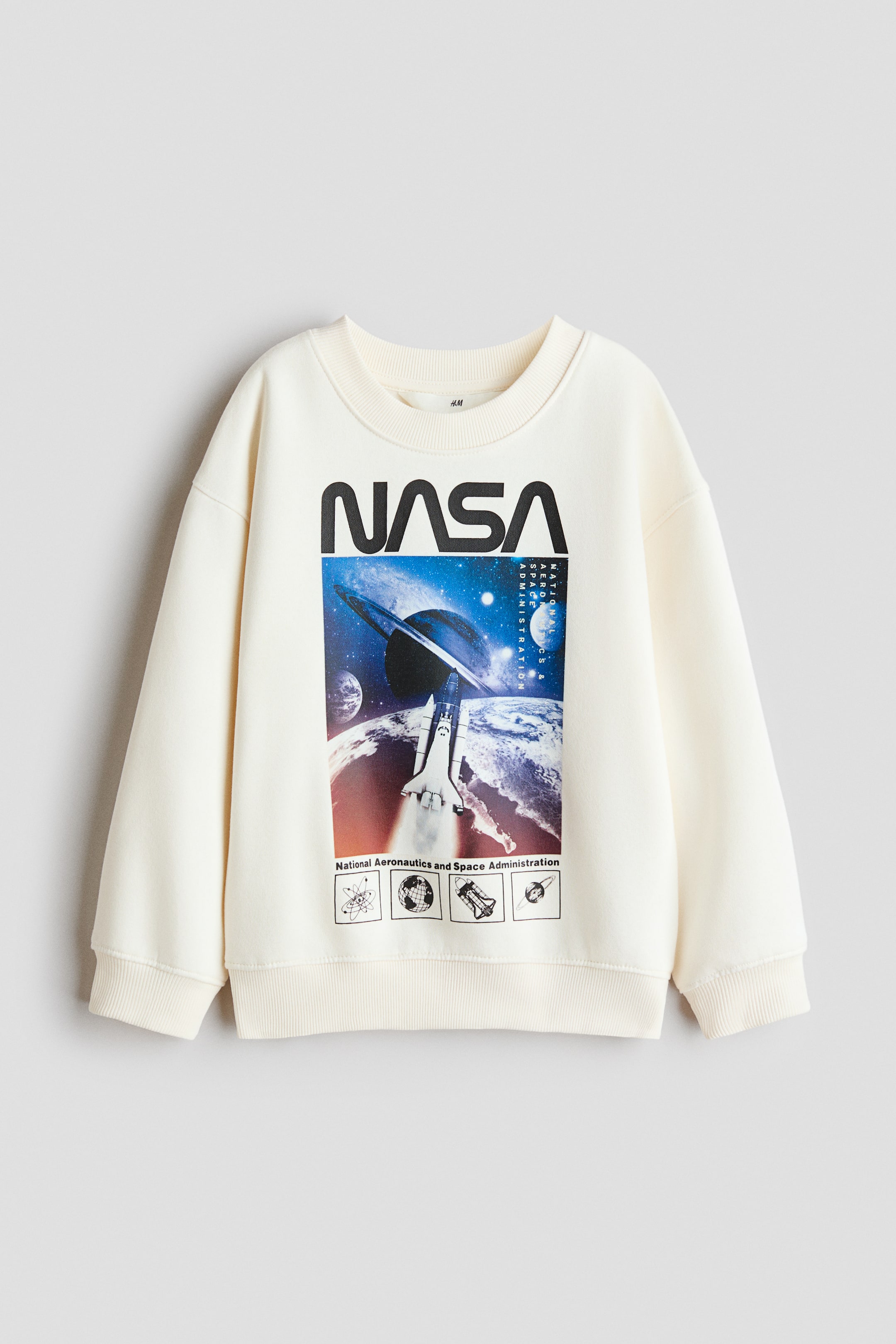 View larger image: A cream-coloured loose-fit sweatshirt is showcasing its front, featuring a large graphic print of the NASA logo above a space scene with a shuttle, planets, and smaller icons. It is designed with a round, ribbed neckline, dropped shoulders, and ribbed trims at the cuffs and hem.