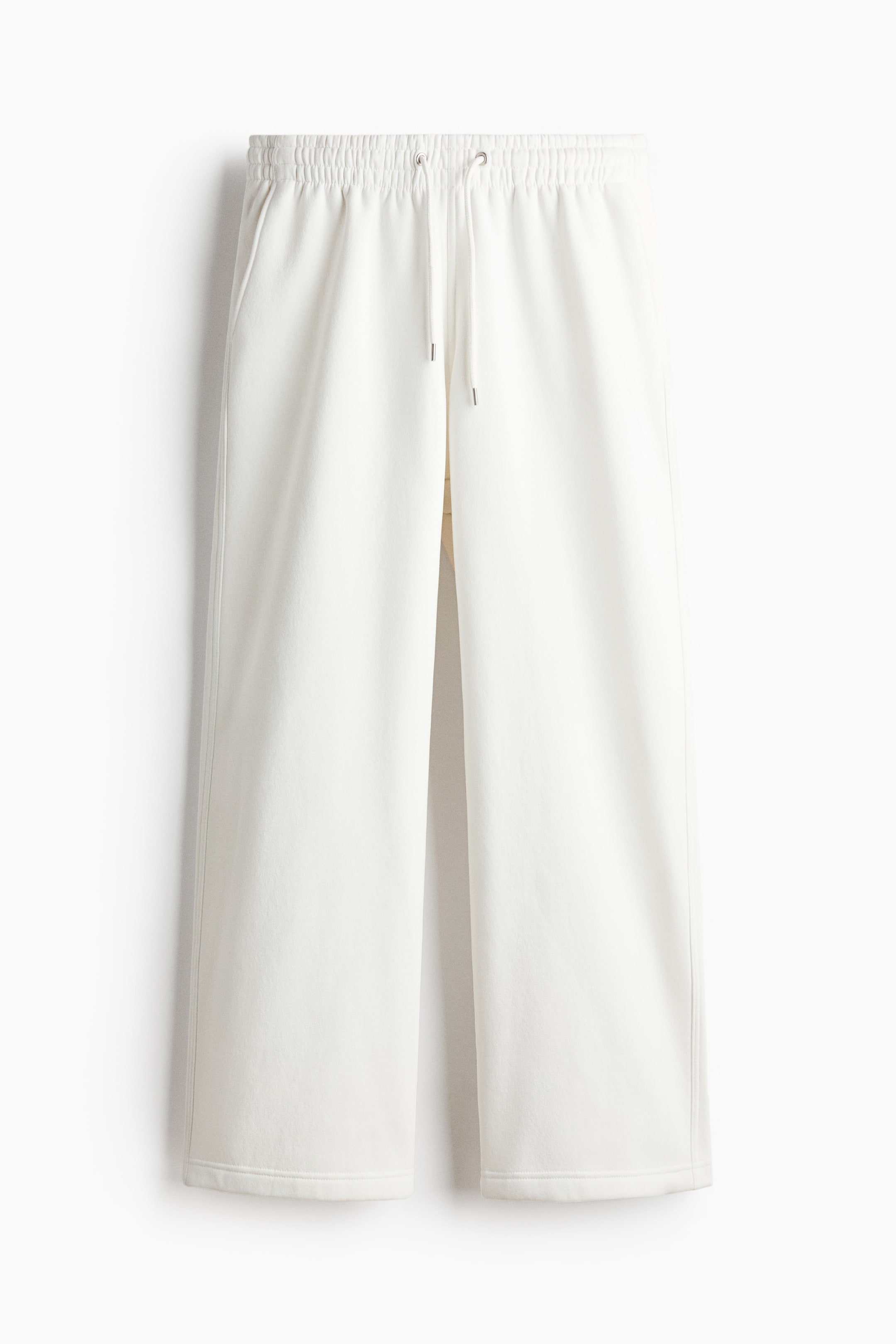 View larger image: White sweatpants feature a covered elasticated waist with a white drawstring and side pockets. They present a loose fit with wide legs ending in straight, open hems.