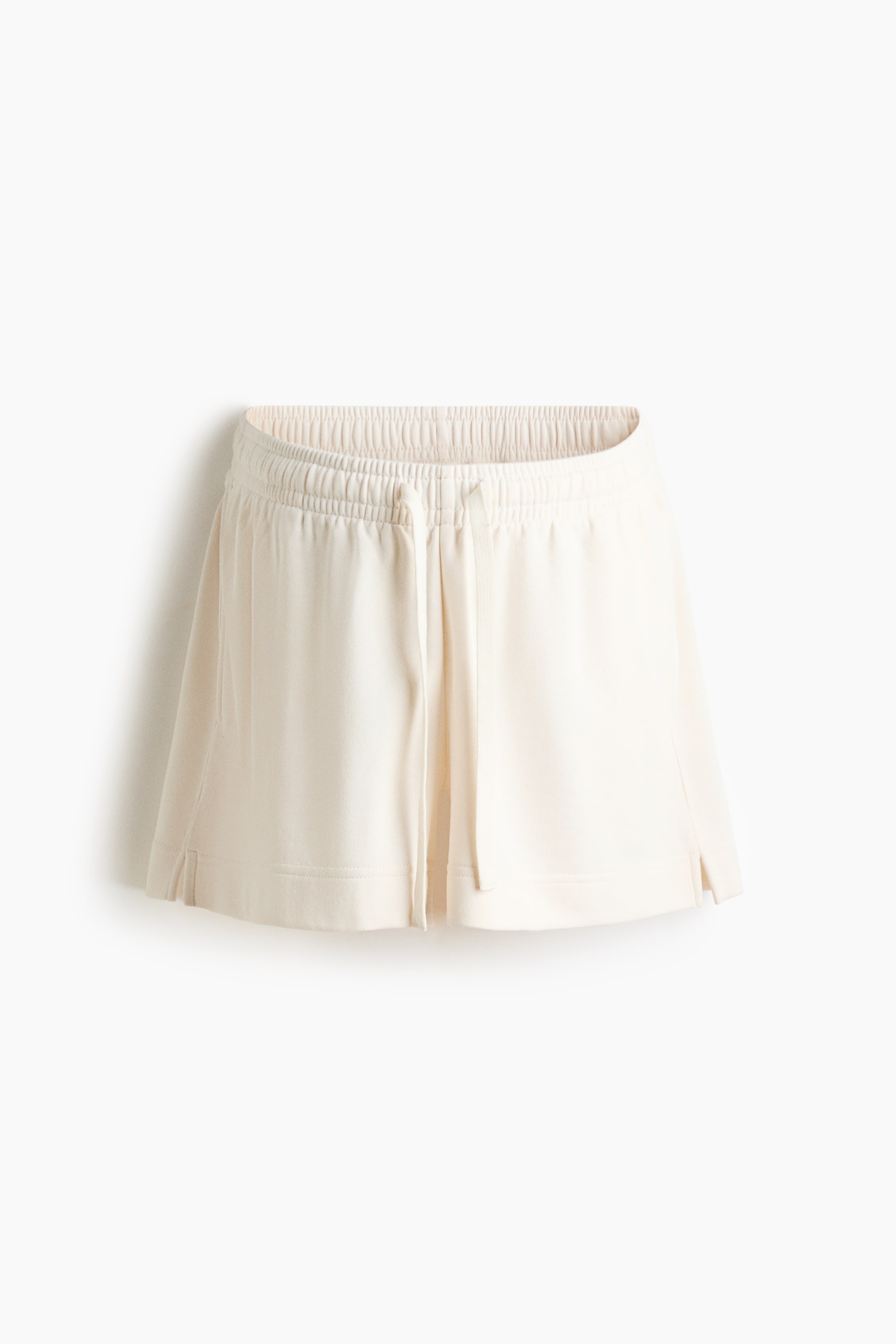 View larger image: "Off-white shorts featuring an elasticated waistband with a visible drawstring at the front, and small side slits at the hem."