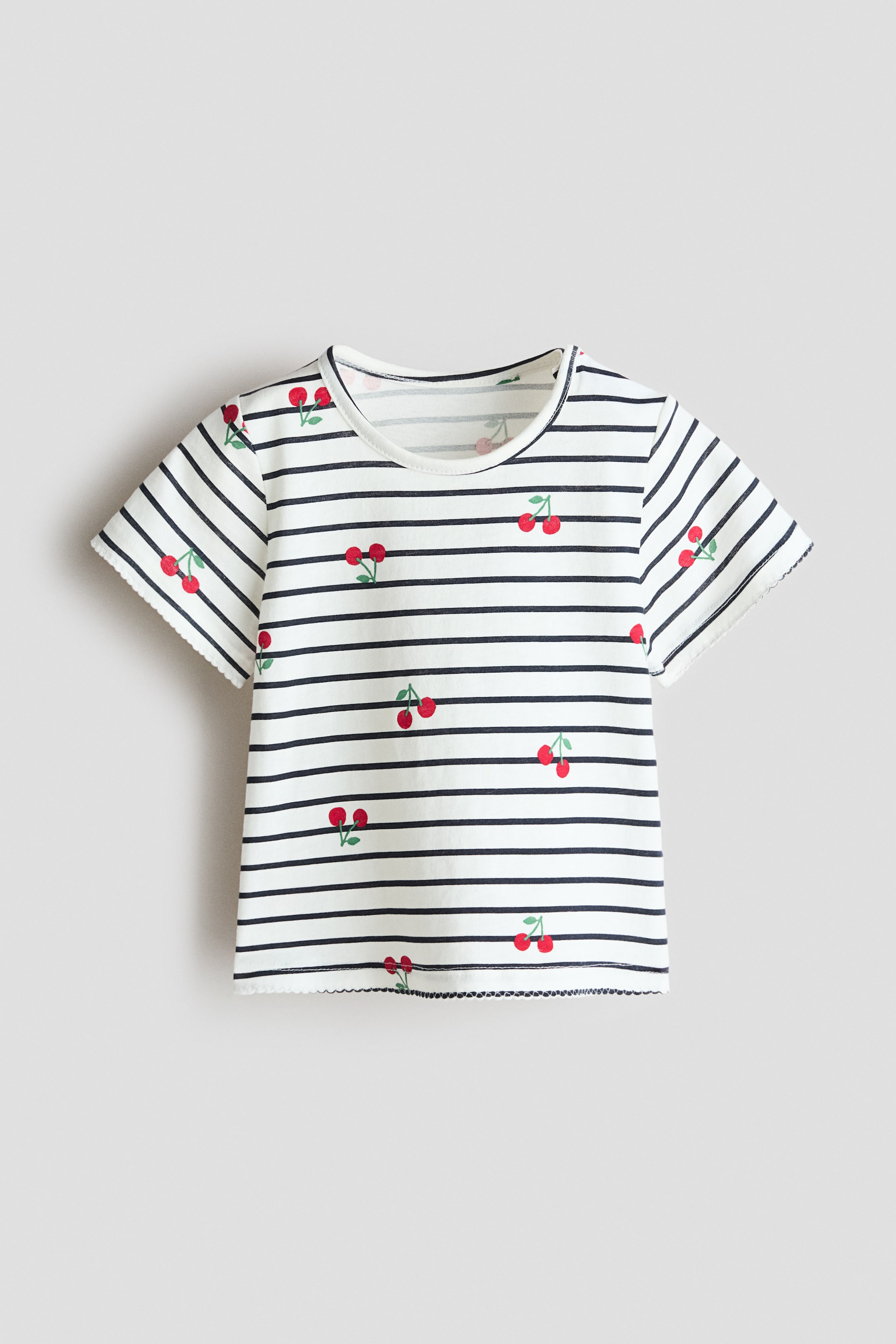 View larger image: The front of the top highlights a soft, printed cotton jersey design, boasting a white base with navy horizontal stripes and scattered red cherry motifs. It is crafted with a round, trimmed neckline and short sleeves, with both the sleeve and bottom hems finished with a delicate picot edge.