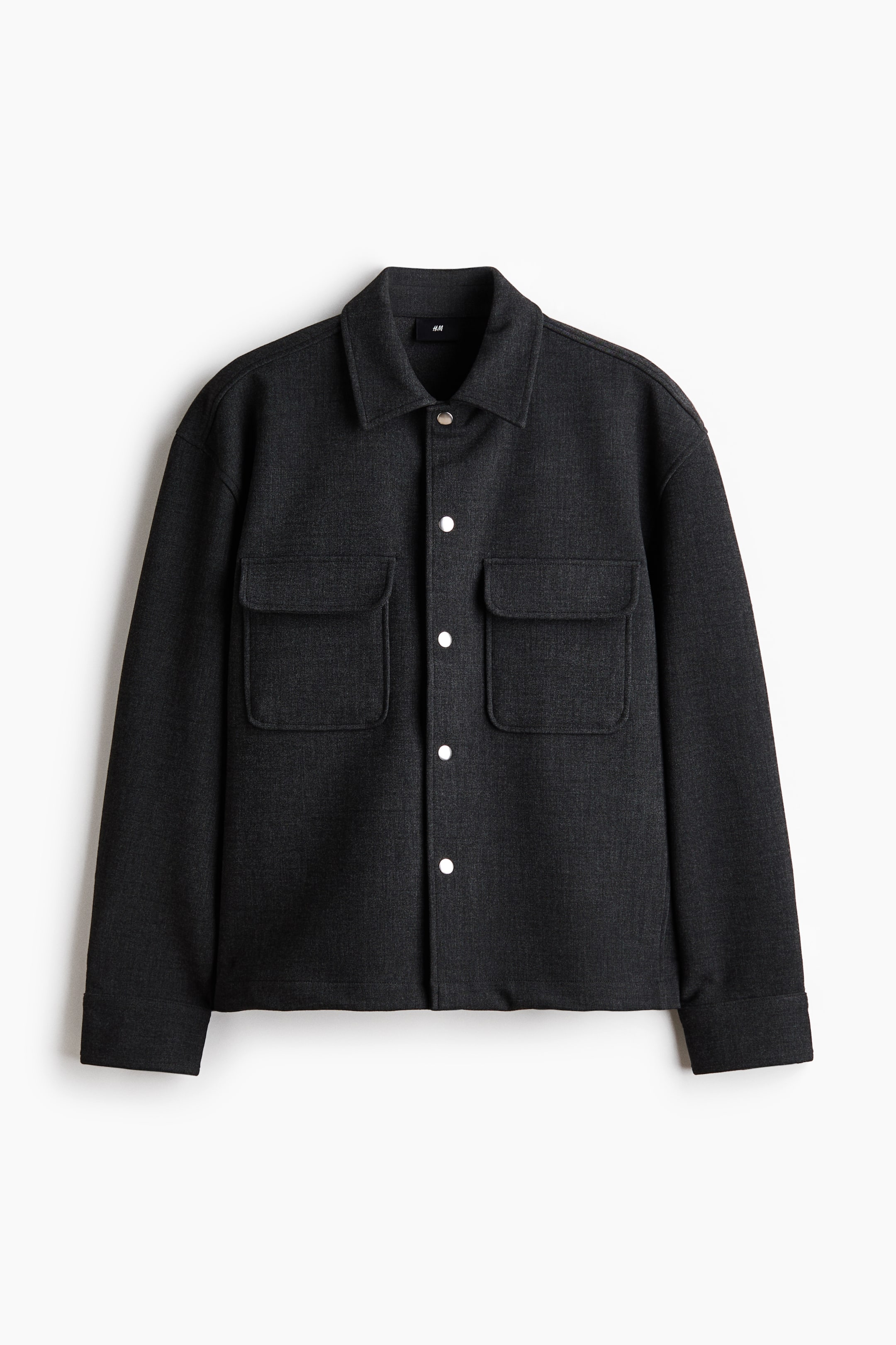 View larger image: A dark grey shacket is facing forward, displaying a pointed collar and a full-length snap-button placket with light-coloured buttons. Two large chest patch pockets with flaps and long sleeves with plain cuffs are also visible.