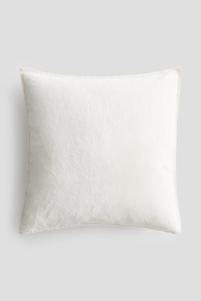 A square off-white cushion is facing front, displaying a soft, plush-textured fabric surface and a subtly stitched border along its edges. - 1