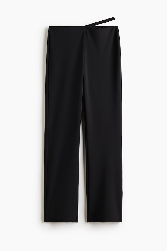 Le pantalon noir est présenté de face. Une ceinture découpée est visible sur le côté gauche, où une fine bande élastique relie deux sections. Le pantalon présente des jambes droites et un tissu lisse. - 1