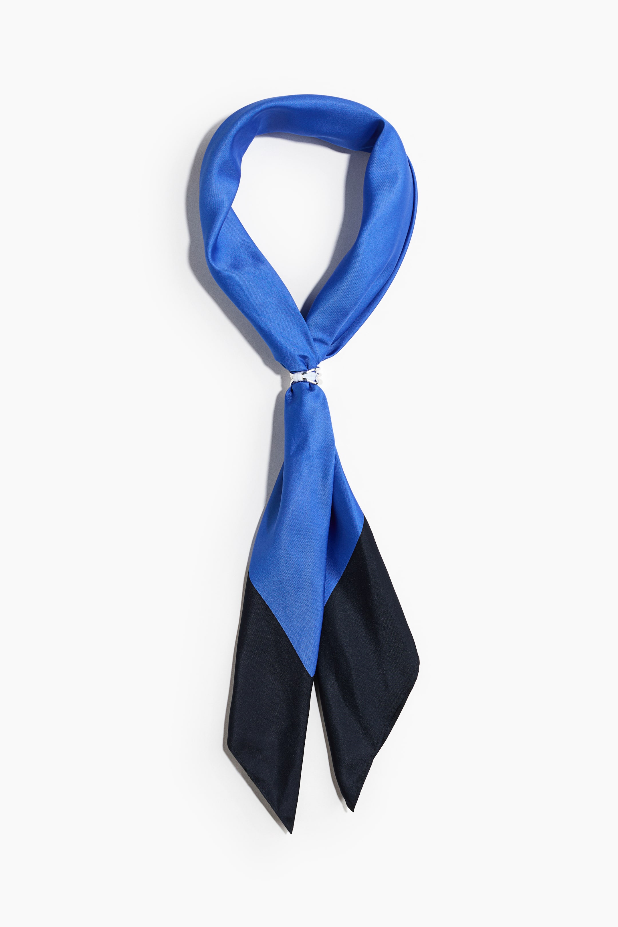 View larger image: A square-neck scarf in woven fabric is shown from the front, styled into a loop and secured with a small, silver-colored metal detail. The color-blocked scarf features a bright blue upper section and pointed black ends hanging down.