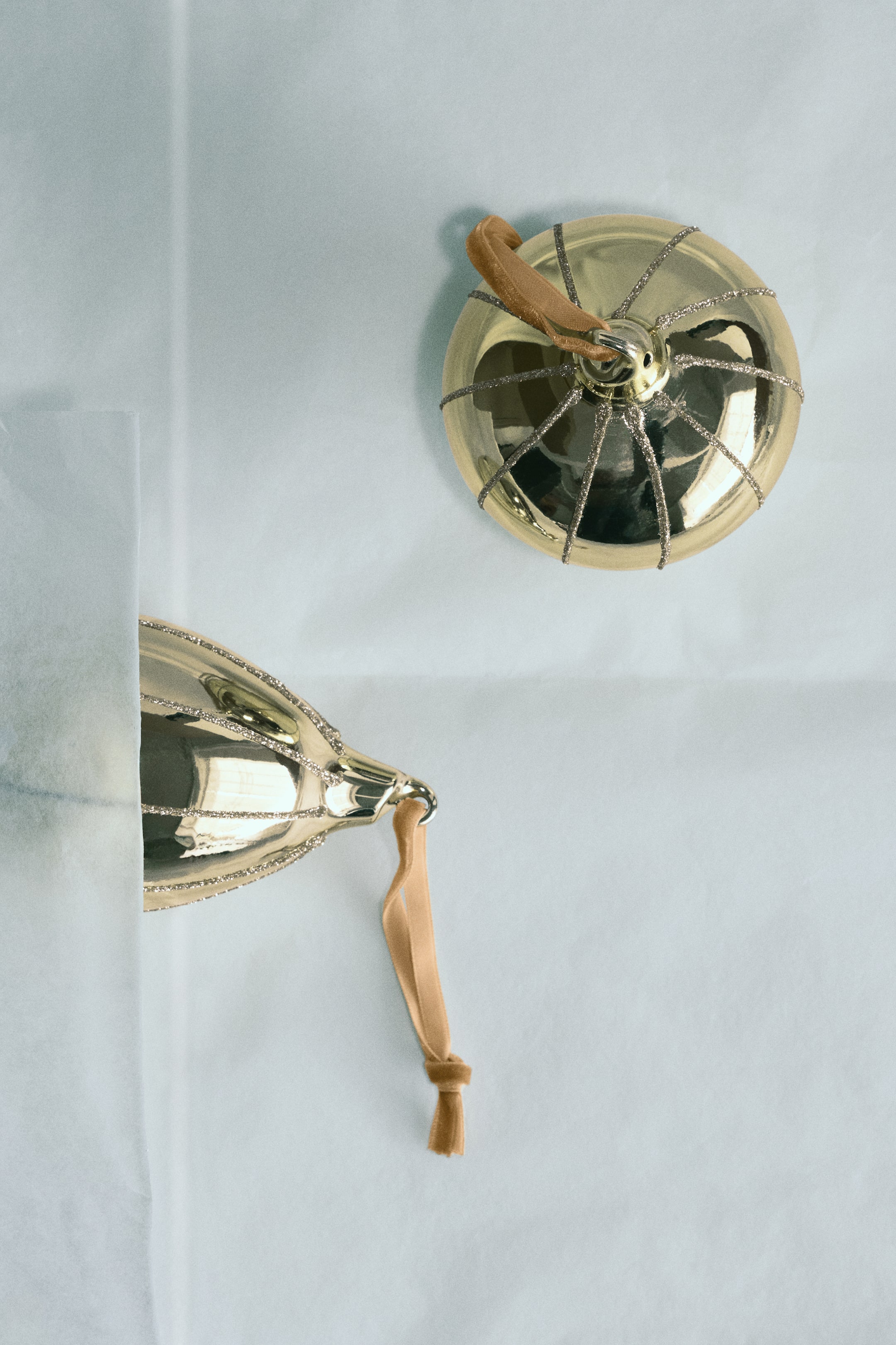 View larger image: Two gold glass ornaments in assorted shapes are shown, featuring a shiny metallic finish with radiating glittery stripes. Each ornament includes a tan velvet hanging loop attached to a metal cap at the top.