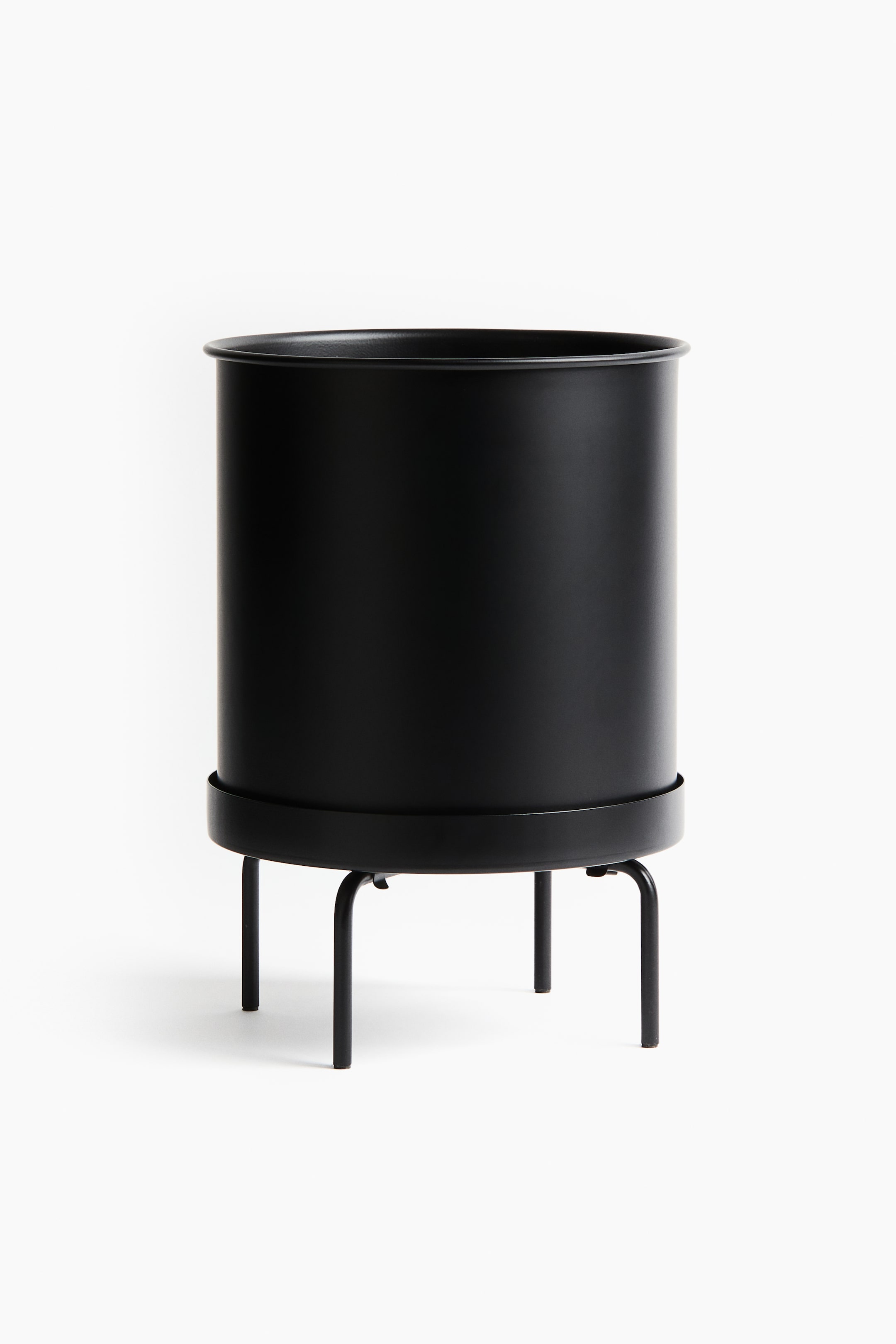 View larger image: A black cylindrical planter rests on a black metal stand. The planter features a subtly rolled rim and sits in a round tray supported by four curved legs.