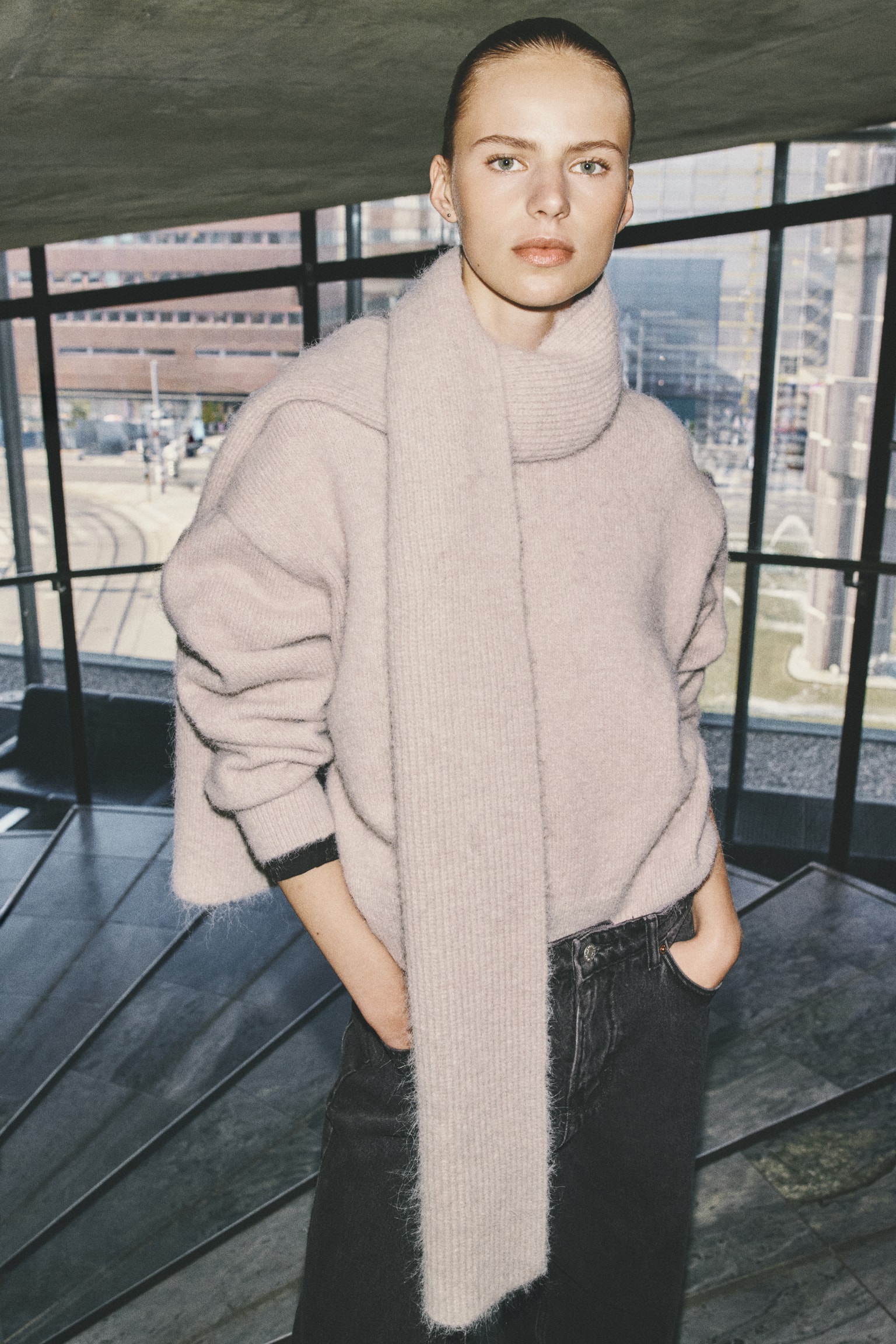 Un pull oversize en maille duveteuse rose pÃ¢le est portÃ© par le mannequin, associÃ© Ã  une longue Ã©charpe cÃ´telÃ©e assortie, enroulÃ©e autour du cou et drapÃ©e sur lâÃ©paule. Le pull prÃ©sente des Ã©paules tombantes et des poignets cÃ´telÃ©s, et il est portÃ© avec un jean gris foncÃ©, le mannequin ayant les mains dans les poches. - 1