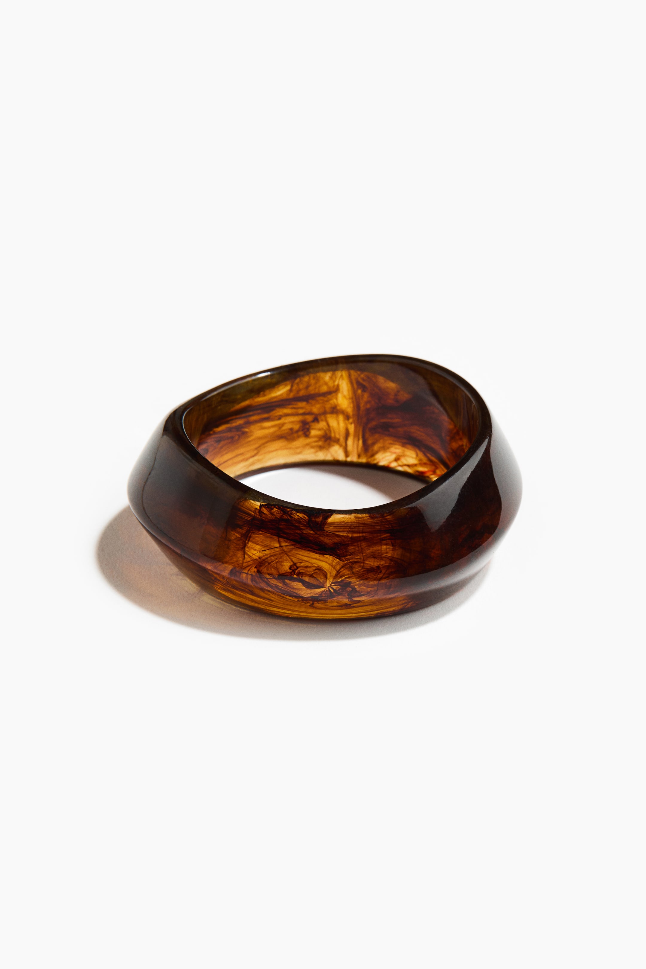View larger image: A chunky bangle is shown from the front, showcasing its glossy, translucent plastic construction. It features an amber-brown color with dark, swirling patterns, and its exterior forms an organic, undulating shape.