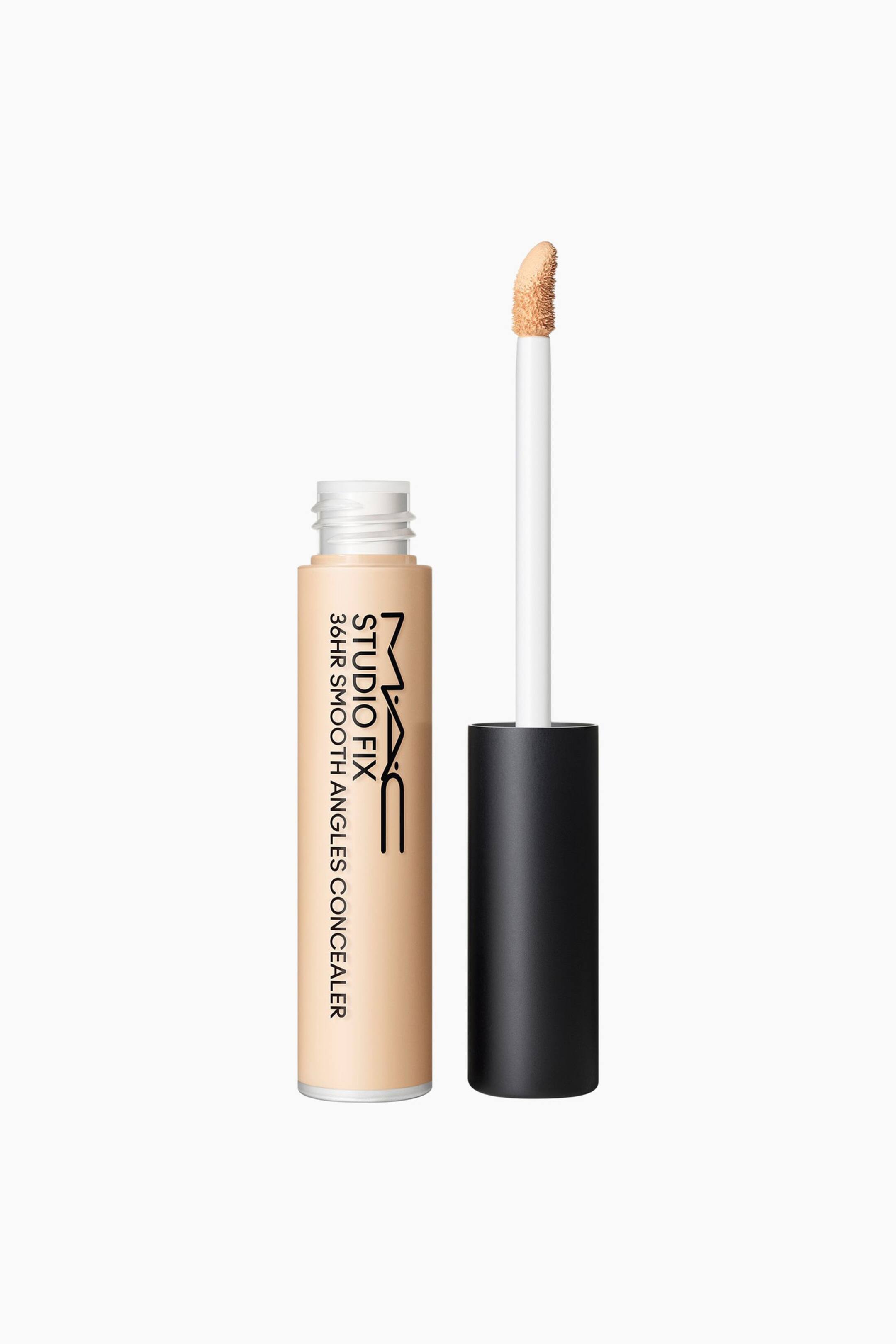 Se større billede: Et lys beige MAC Studio Fix 36HR Smooth Angles Concealer-rør står oprejst, vendt fremad, med toppen åben og den hvide skruegevind synlig. Den sorte hætte ligger ved siden af røret, og en hvid applikatorstav med en lys beige concealer-betrukket svampespids er placeret oprejst ved siden af det åbne rør.