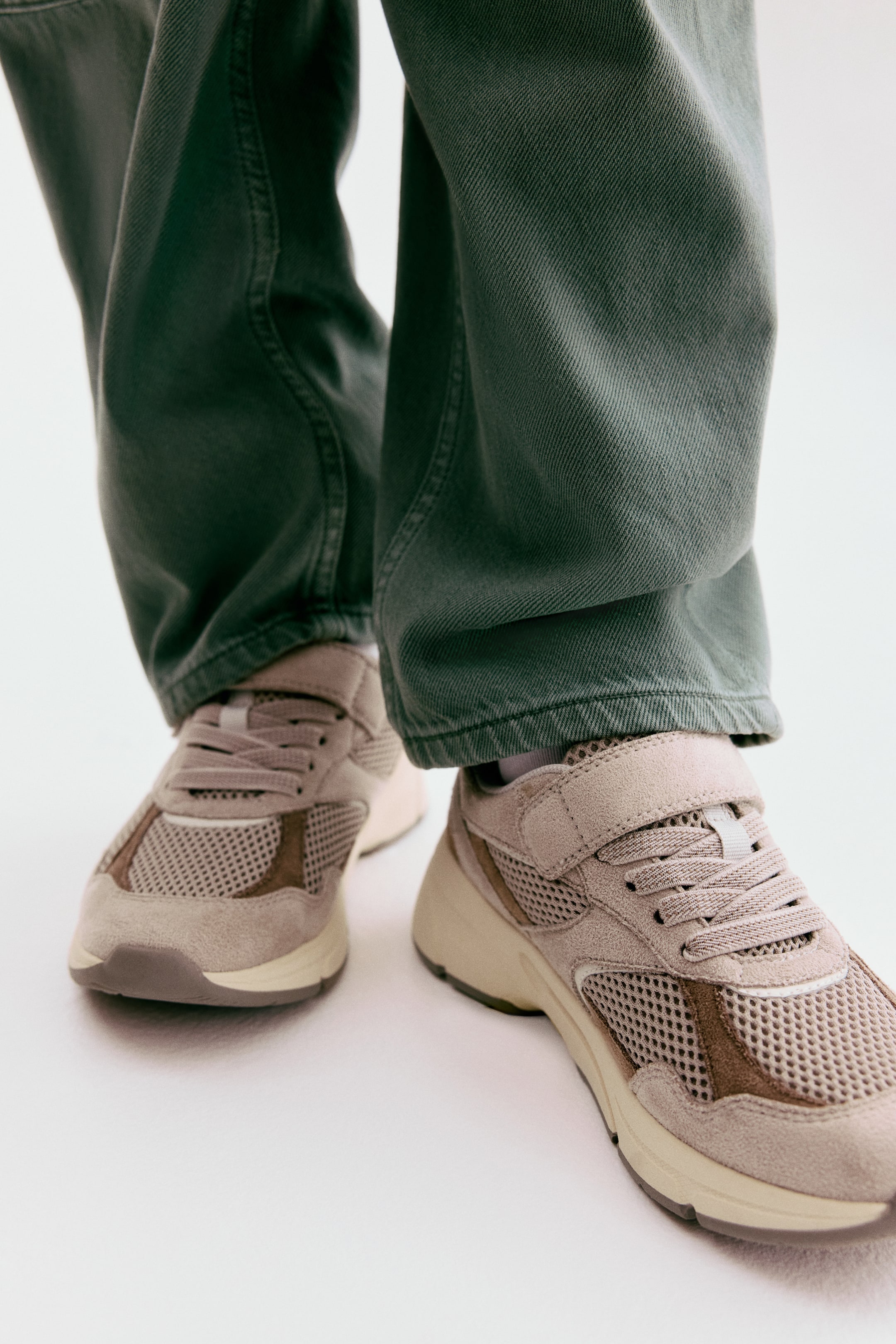 View larger image: Trainers feature greige mesh panels and suede-like overlays with darker brown accents, showcasing a chunky sole and a combination of laces and a hook-and-loop strap across the instep.