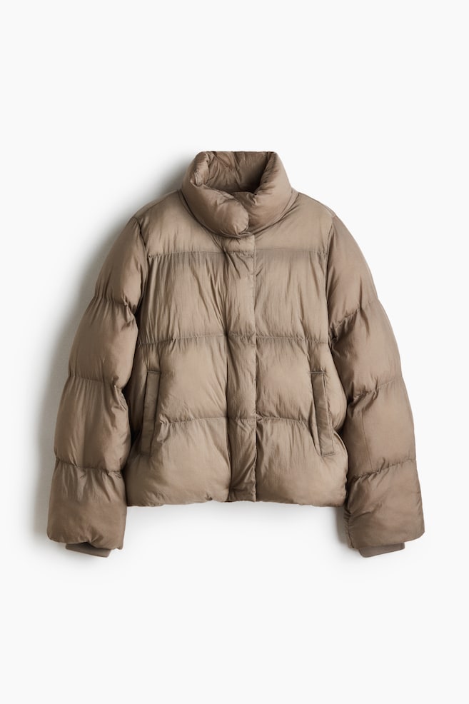 A taupe-colored puffer jacket is facing front, showcasing a high stand-up collar and wide horizontal quilted panels. The jacket is featuring a hidden front closure, two side welt pockets, and long sleeves with elasticated cuffs. - 1