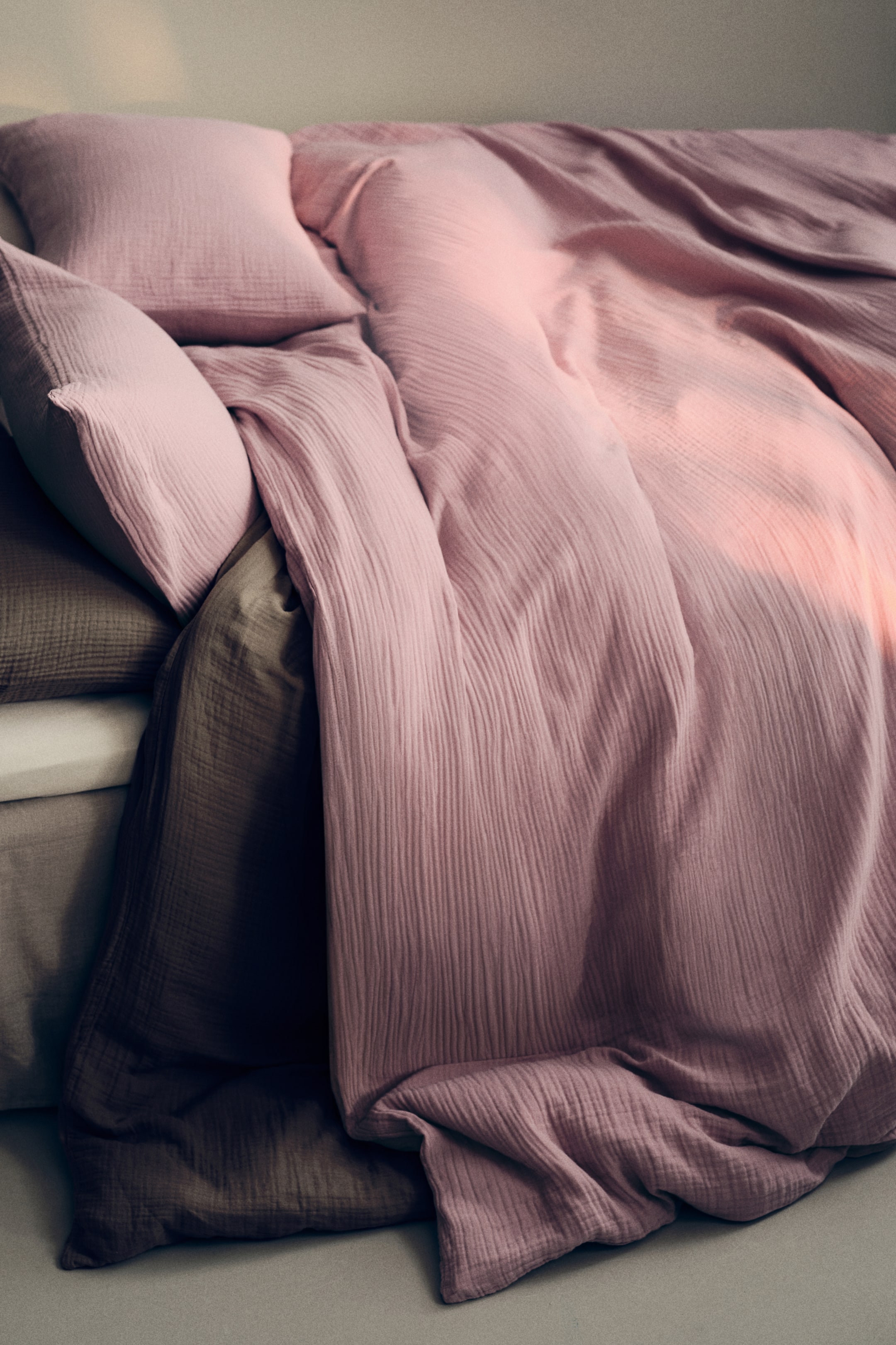 View larger image: Pink crinkled bedding, comprising a duvet cover and two pillows, is elegantly draped over a deeper brown bedding layer. The duvet cover forms gentle folds, while the pillows rest against it, highlighting their textured fabric.