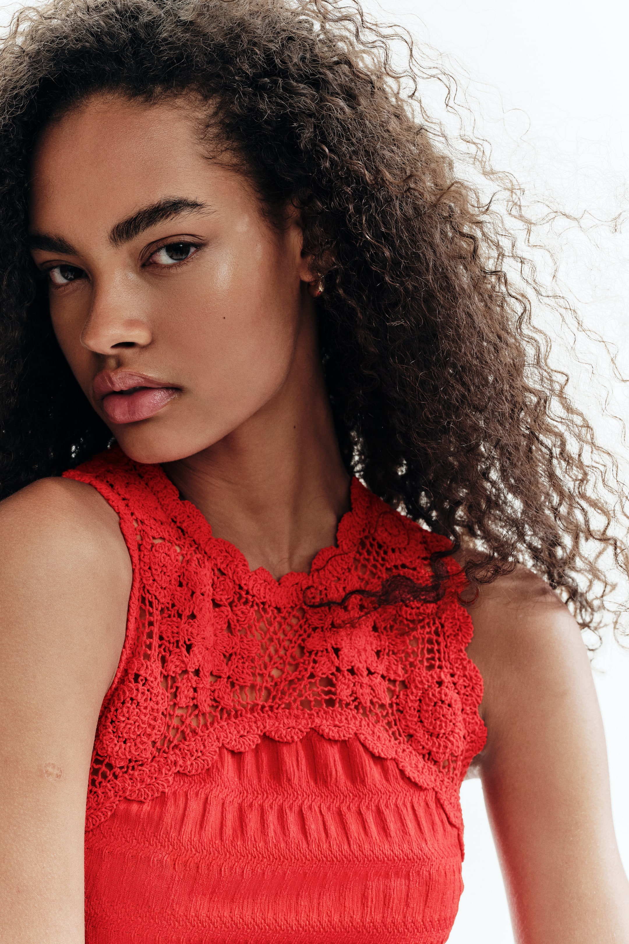 Ampliar la imagen: Un top sin mangas de color rojo presenta un escote de crochet ancho y festoneado. La parte superior del corpiño muestra un trabajo de crochet intrincado, mientras que la sección inferior visible exhibe una textura fruncida horizontalmente.