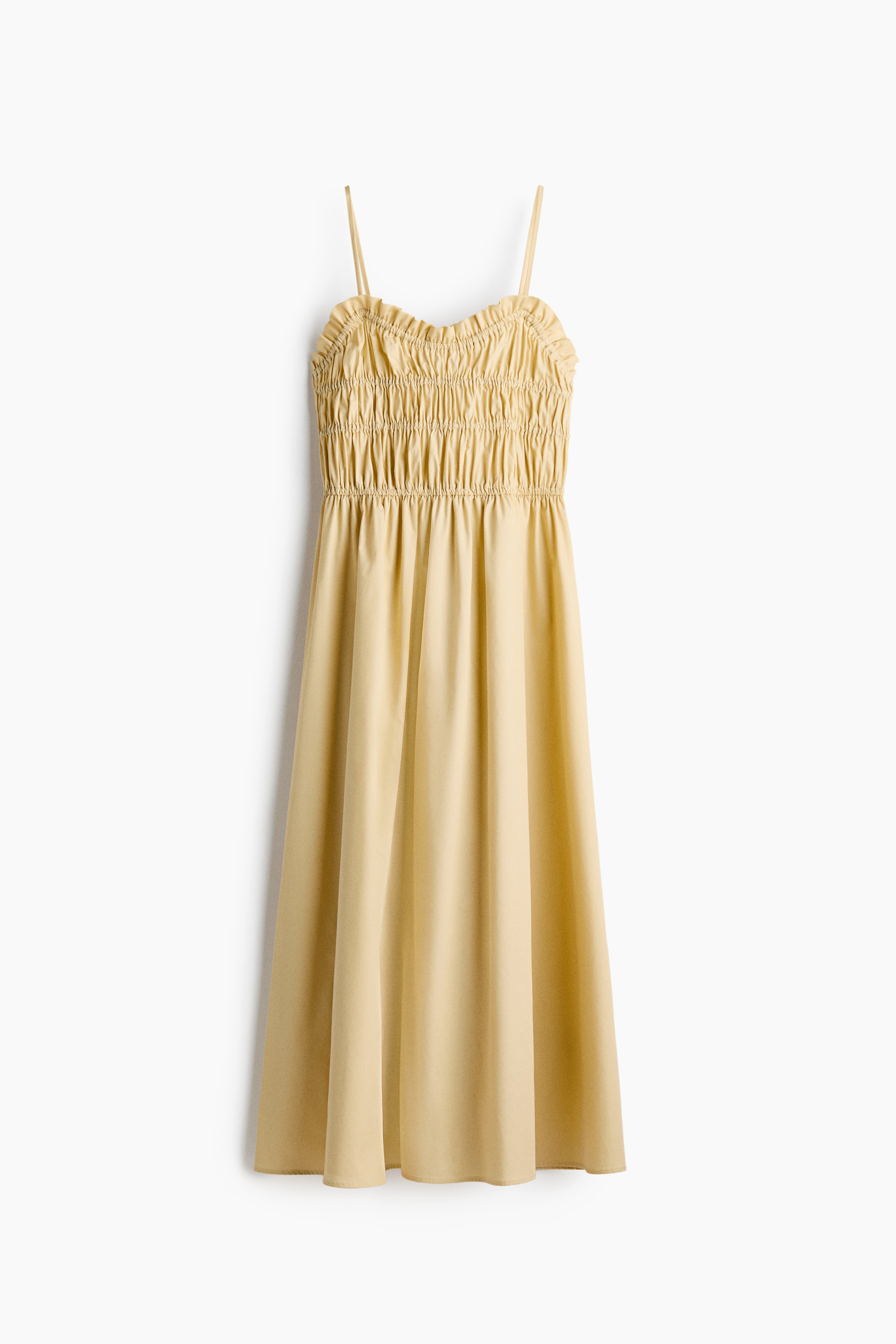 A light yellow, calf-length dress is worn by the model, featuring a ruched bodice with horizontal elasticated seams, thin shoulder straps, and a flared, flowing skirt. The model is standing and posing in the dress, which is styled with black pointed-toe flat shoes.