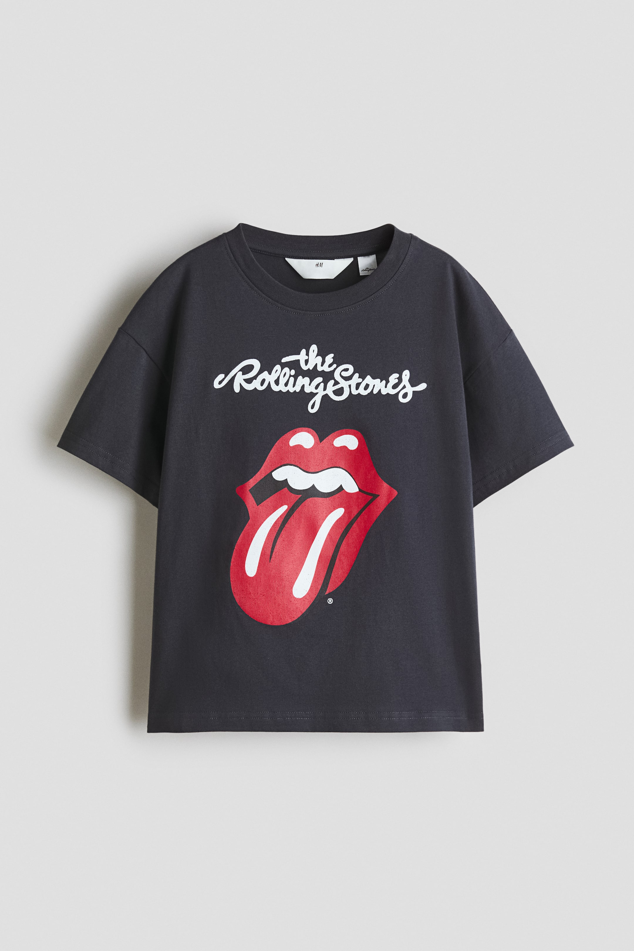 View larger image: A charcoal grey t-shirt featuring a ribbed crew neck and short sleeves, with "The Rolling Stones" in white script above a large red and white tongue and lips logo on the front.