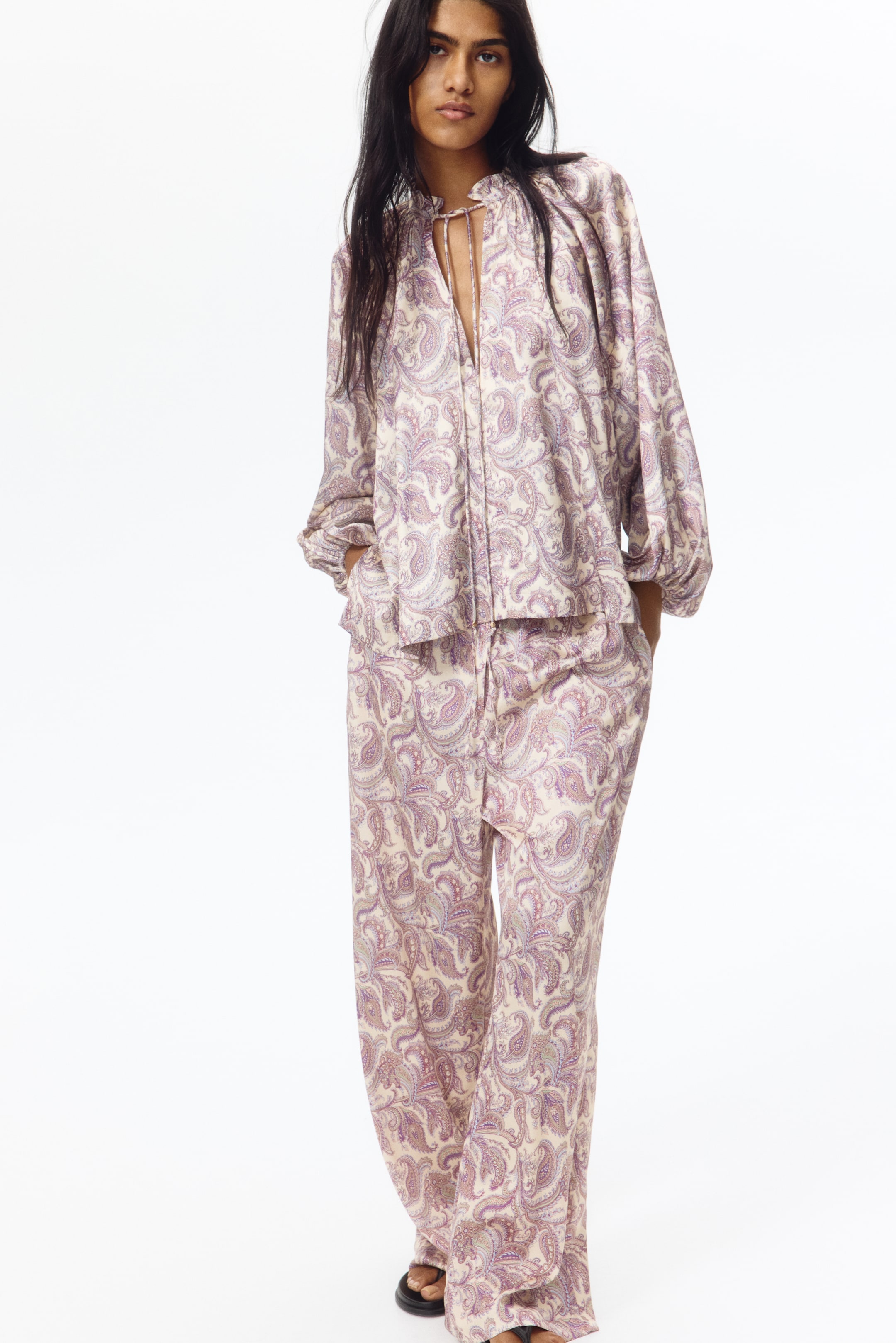 View larger image: A two-piece paisley patterned set, featuring a top and wide-leg pants, is showcasing a ruffled drawstring neckline with a V-neck opening and long, voluminous sleeves with gathered cuffs on the top. The matching pants are exhibiting a relaxed, wide-leg fit.