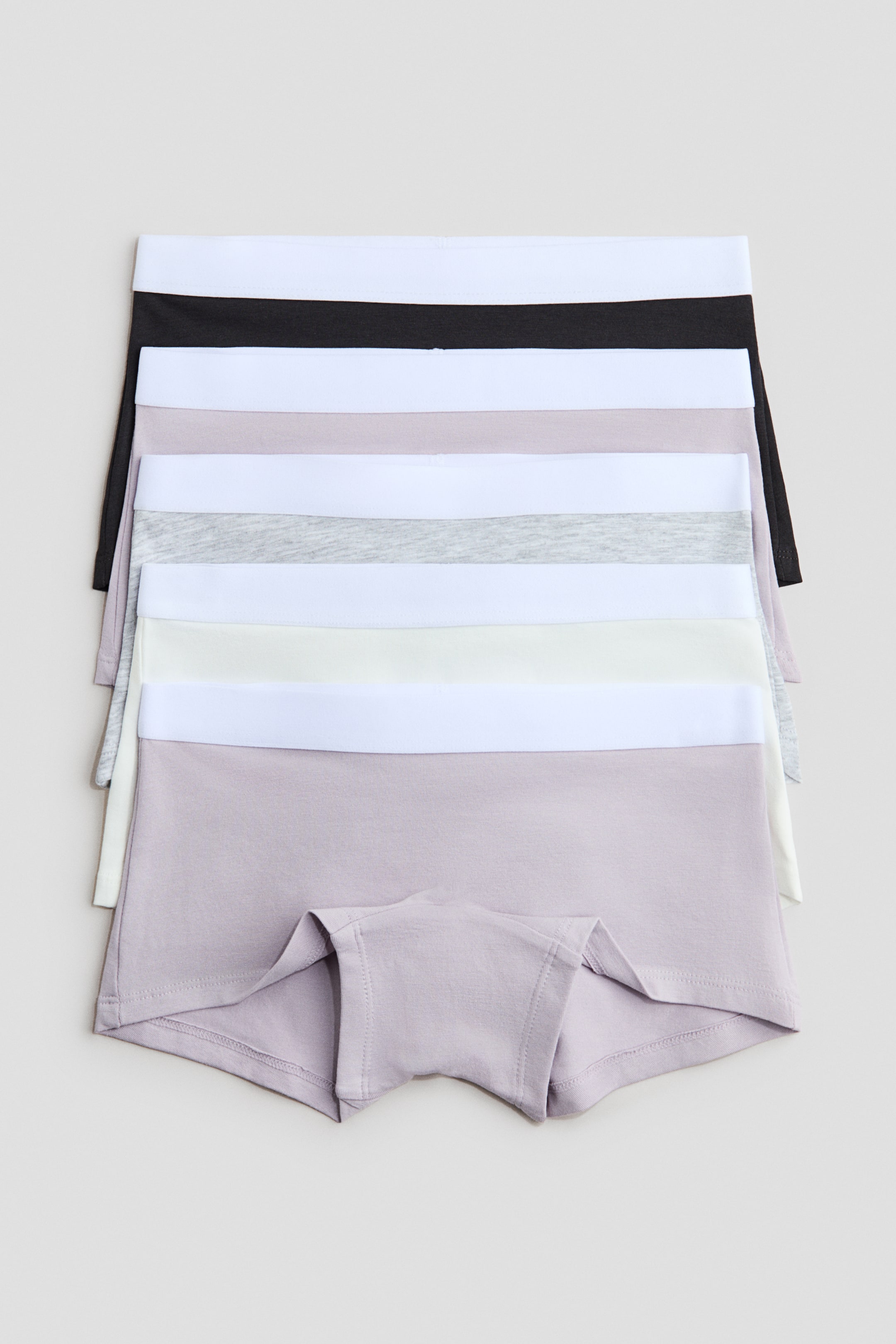 Se større billede: Boxershorts i bomuldsjersey præsenteres i en stak fra forsiden. De har elastiske taljer og foret skridt, og de fremviser forskellige neutrale farver, herunder sort, hvid, lysegrå og lavendel.