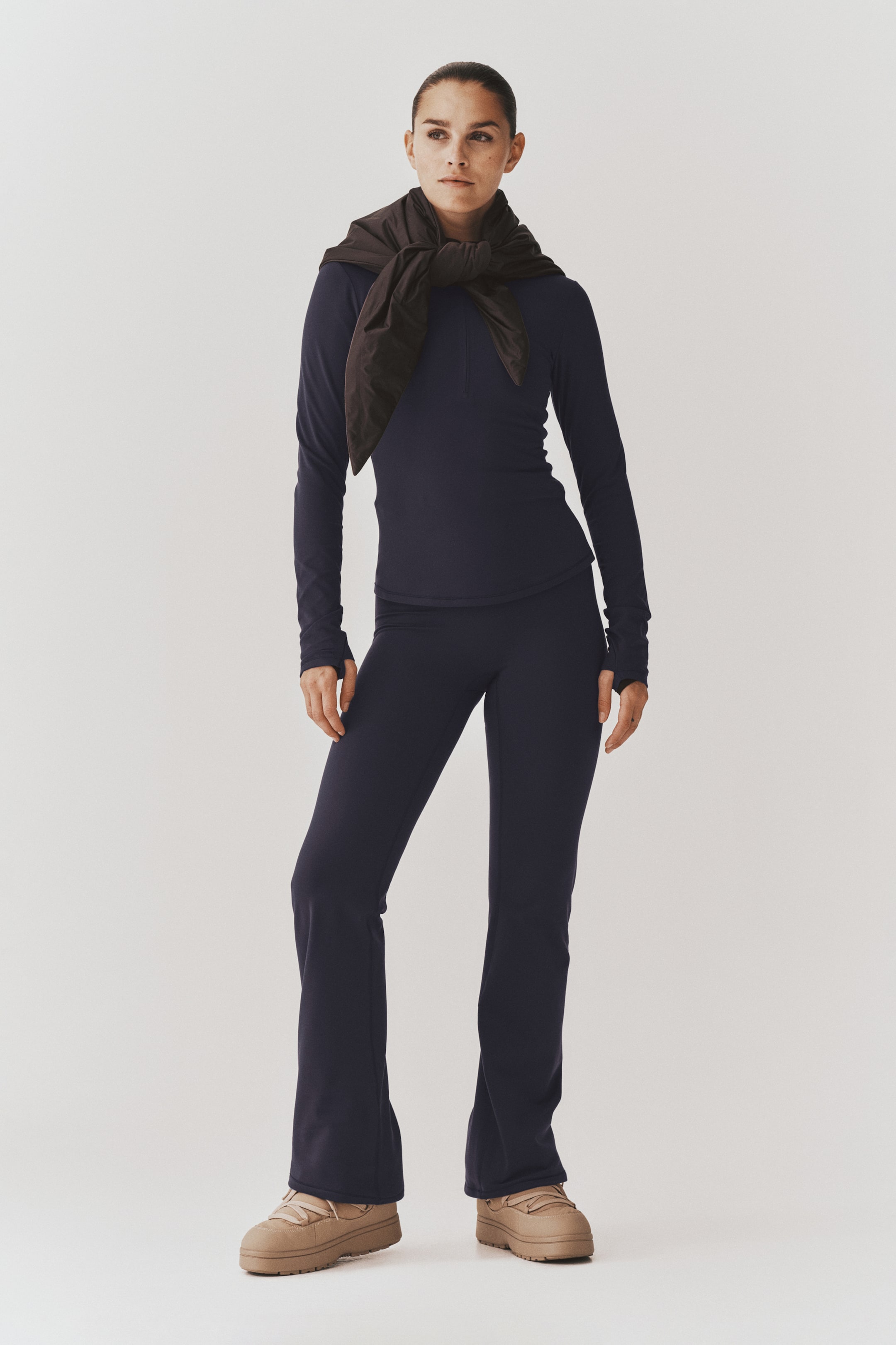 View larger image: A dark navy blue athletic set, consisting of a long-sleeve top and matching flared pants, is being worn by the model. The fitted top features thumbholes at the cuffs, while the high-waisted pants are slim through the leg and flare slightly at the hem.