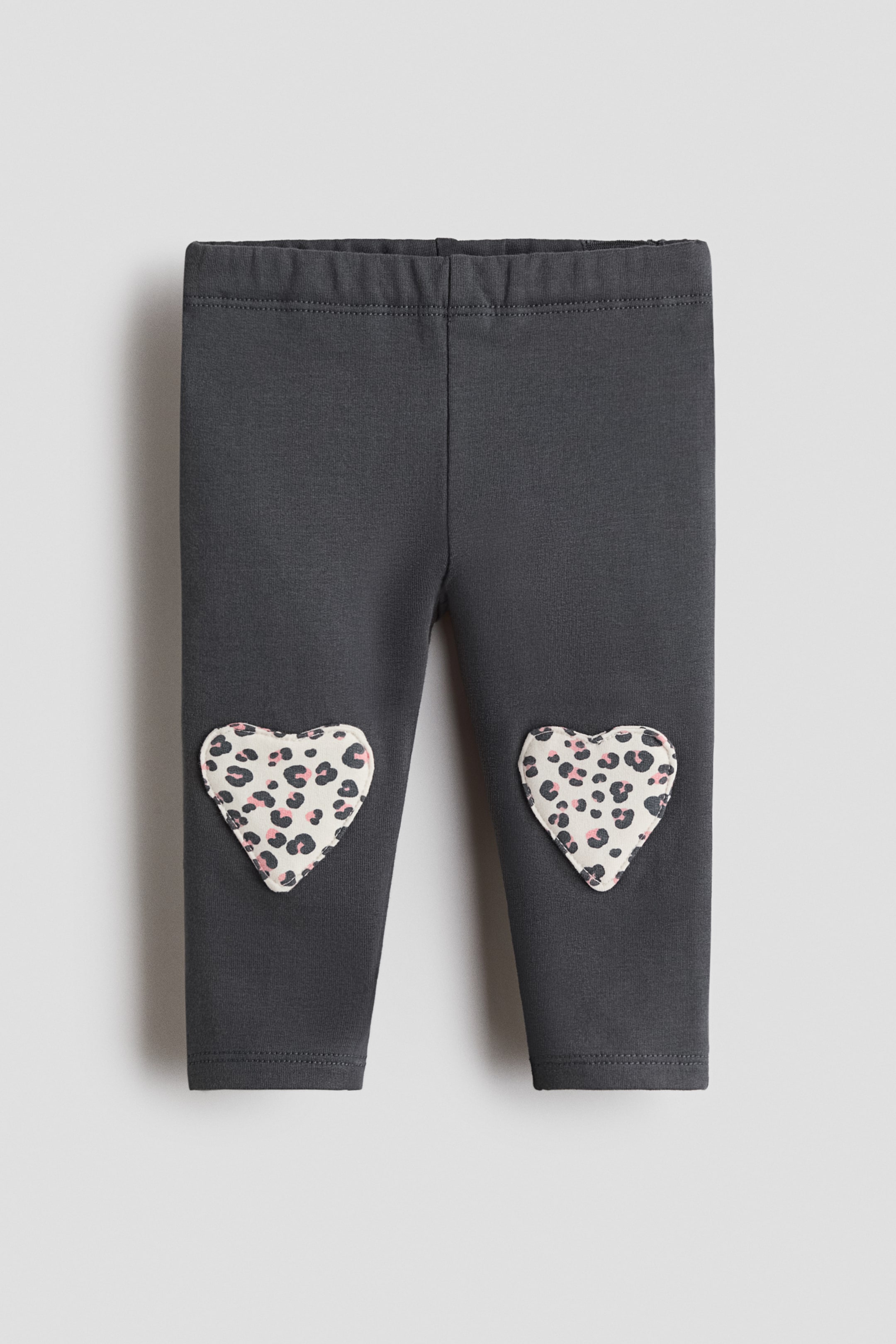 View larger image: Dark gray leggings feature an elasticized waistband and two heart-shaped patches on the knees. The patches show a leopard print design with black and pink spots on a cream base.