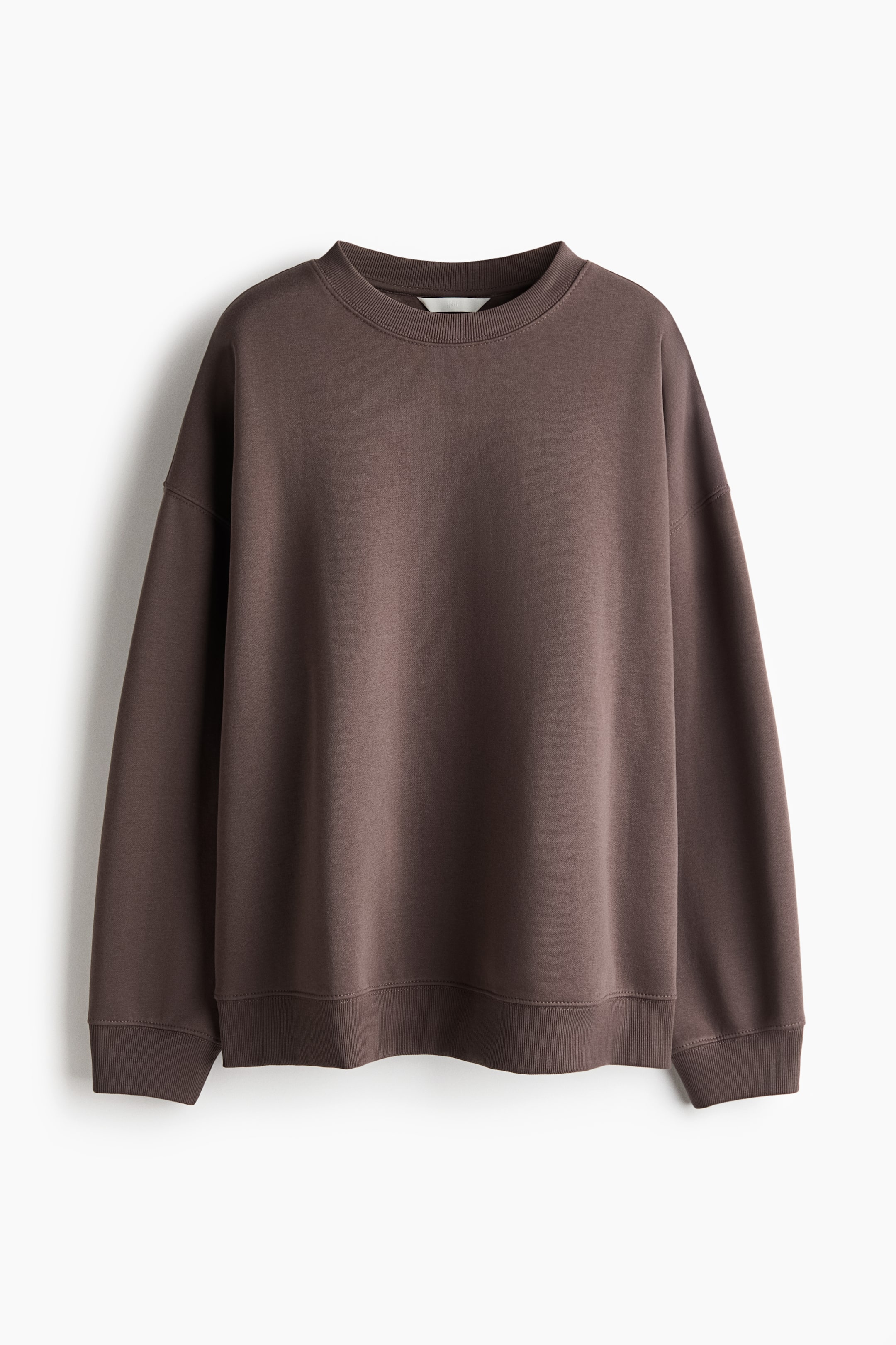 Visa större bild: En oversized brun sweatshirt hänger i frontvy och visar en ribbad rund halsringning, nedhasade axlar och långa ärmar. Plagget har en avslappnad passform med ribbade detaljer vid ärmsluten och fållen.