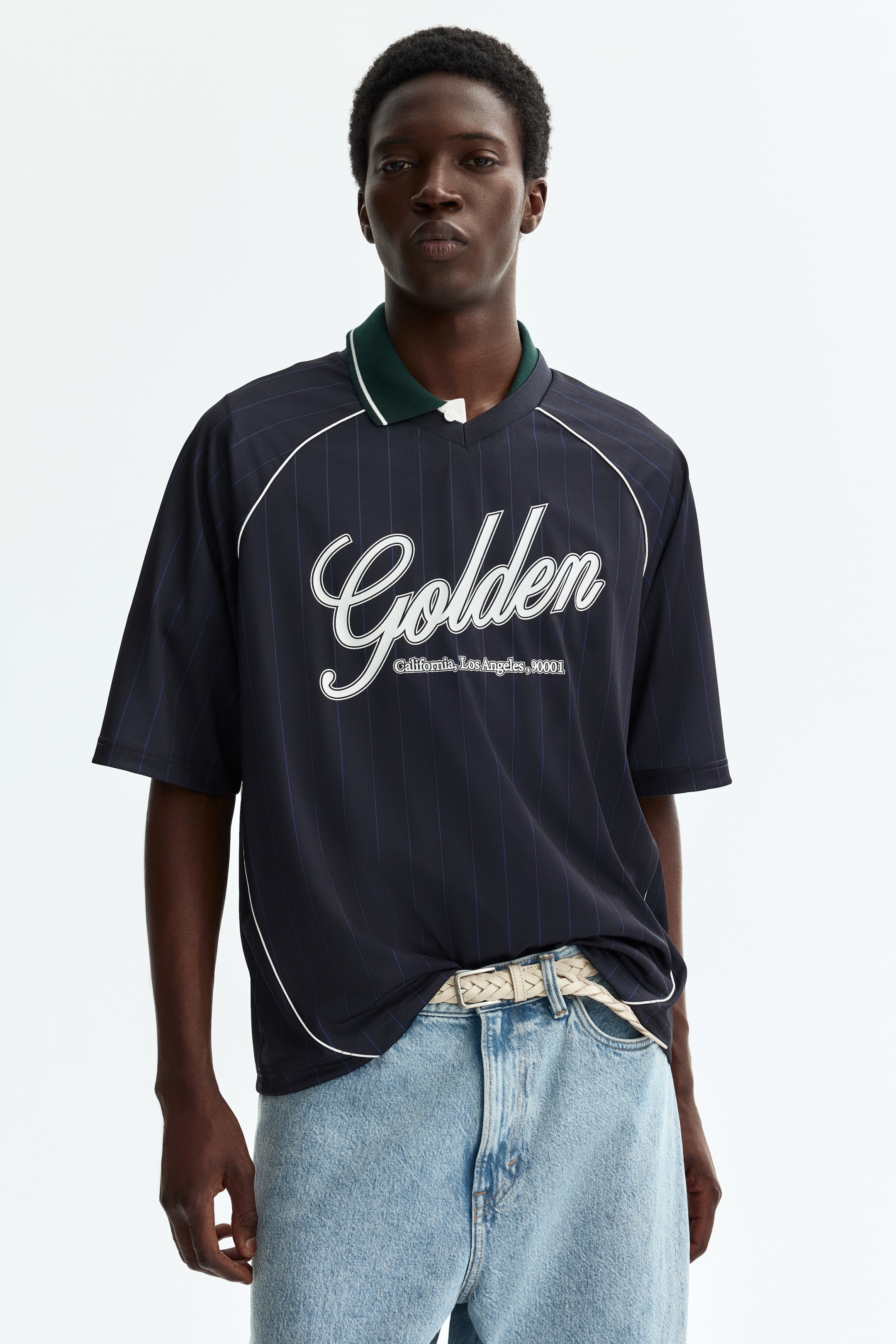 Agrandir l'image: Un polo à manches courtes bleu marine, vu de face, présente de fines rayures verticales et un col polo vert foncé avec un liseré blanc. Le polo affiche "Golden" en écriture blanche sur la poitrine, suivi de "California, Los Angeles, 90001" en texte plus petit en dessous, et des passepoils blancs détaillant les coutures des manches raglan.