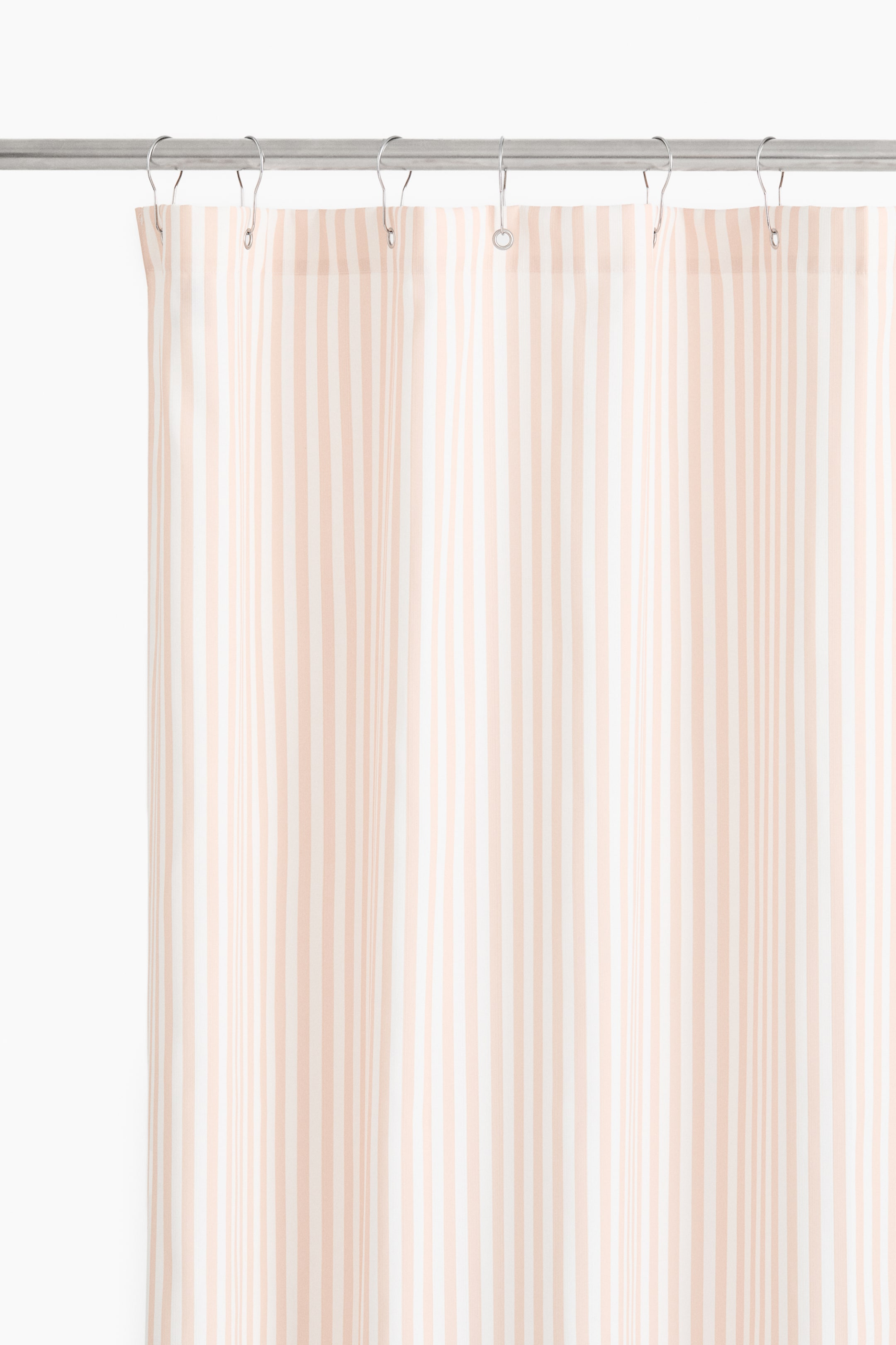 View larger image: A striped shower curtain hangs from a silver rod, showcased from the front. It features alternating light peach and white vertical stripes with a textured finish, and metal eyelets are visible along the top edge, through which silver shower curtain rings are hooked.