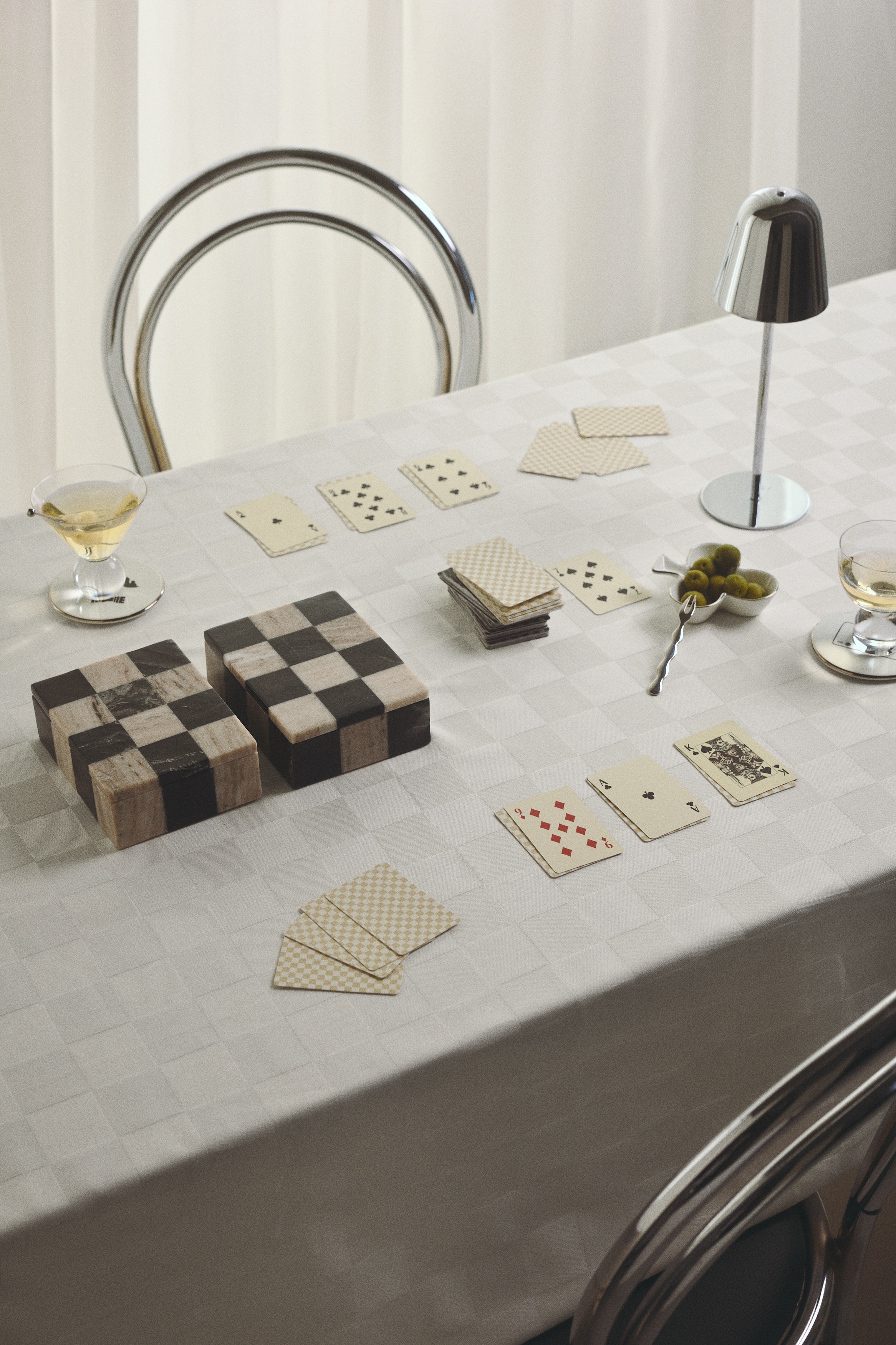 Una scatola quadrata in marmo con un motivo a scacchiera nero e crema Ã¨ appoggiata con il coperchio leggermente aperto. Diverse carte da gioco sono sparse davanti alla scatola e mostrano vari semi e figure.