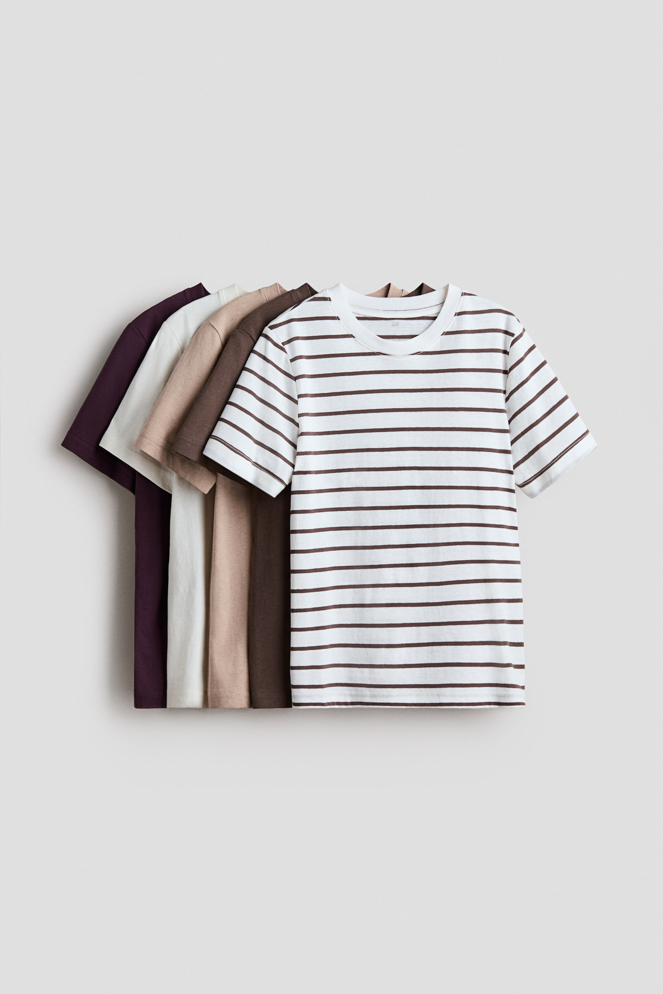 View larger image: Presenting a collection of soft cotton jersey t-shirts. The t-shirt at the forefront features a white background with brown horizontal stripes, a round neckline, and a straight-cut hem. Behind it, solid-colored t-shirts are layered in shades of deep purple, cream, light brown, and dark brown, each also showcasing a round neckline and a straight-cut hem.