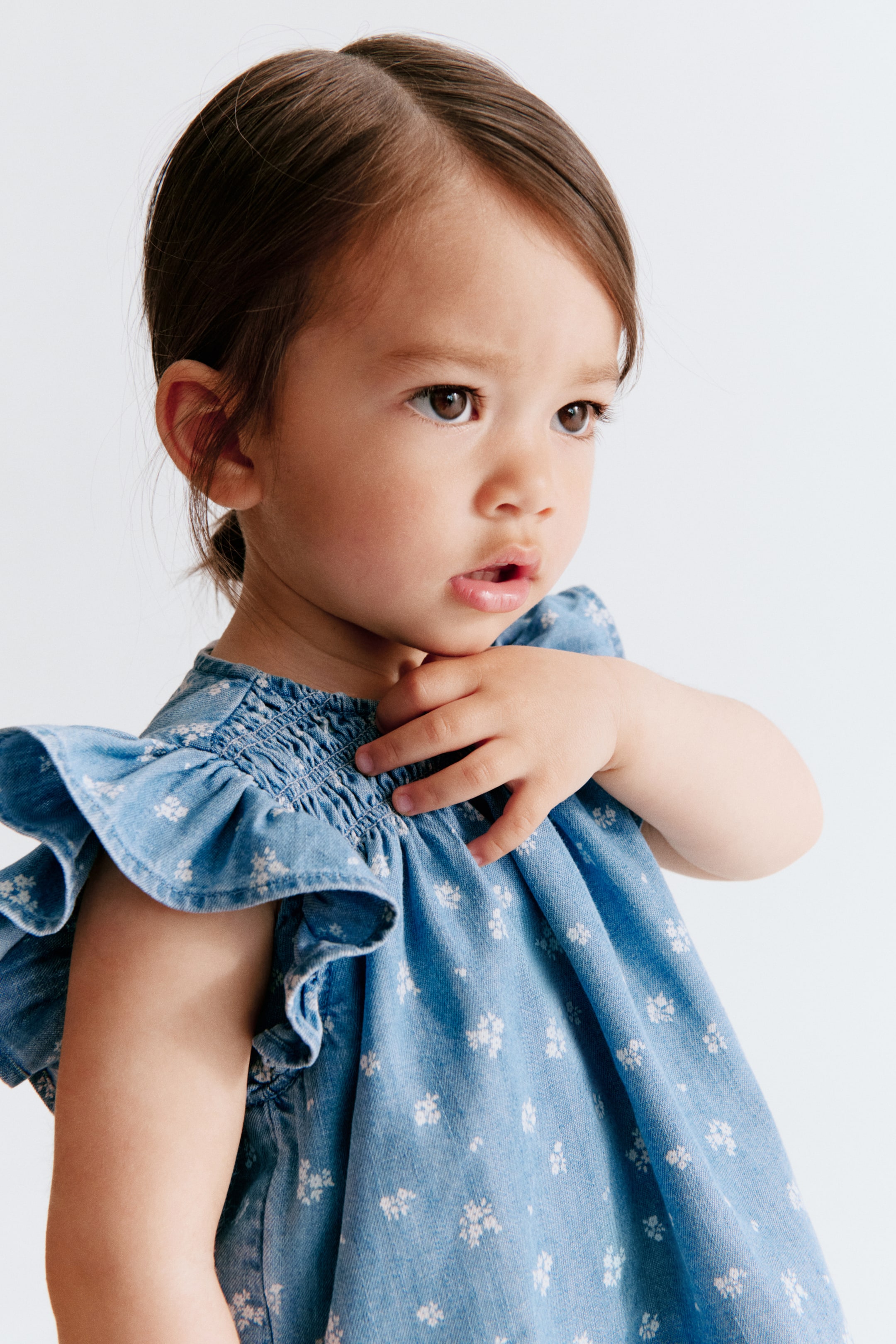 View larger image: A blue denim dress featuring a white floral pattern, a smocked bodice, and ruffled cap sleeves.