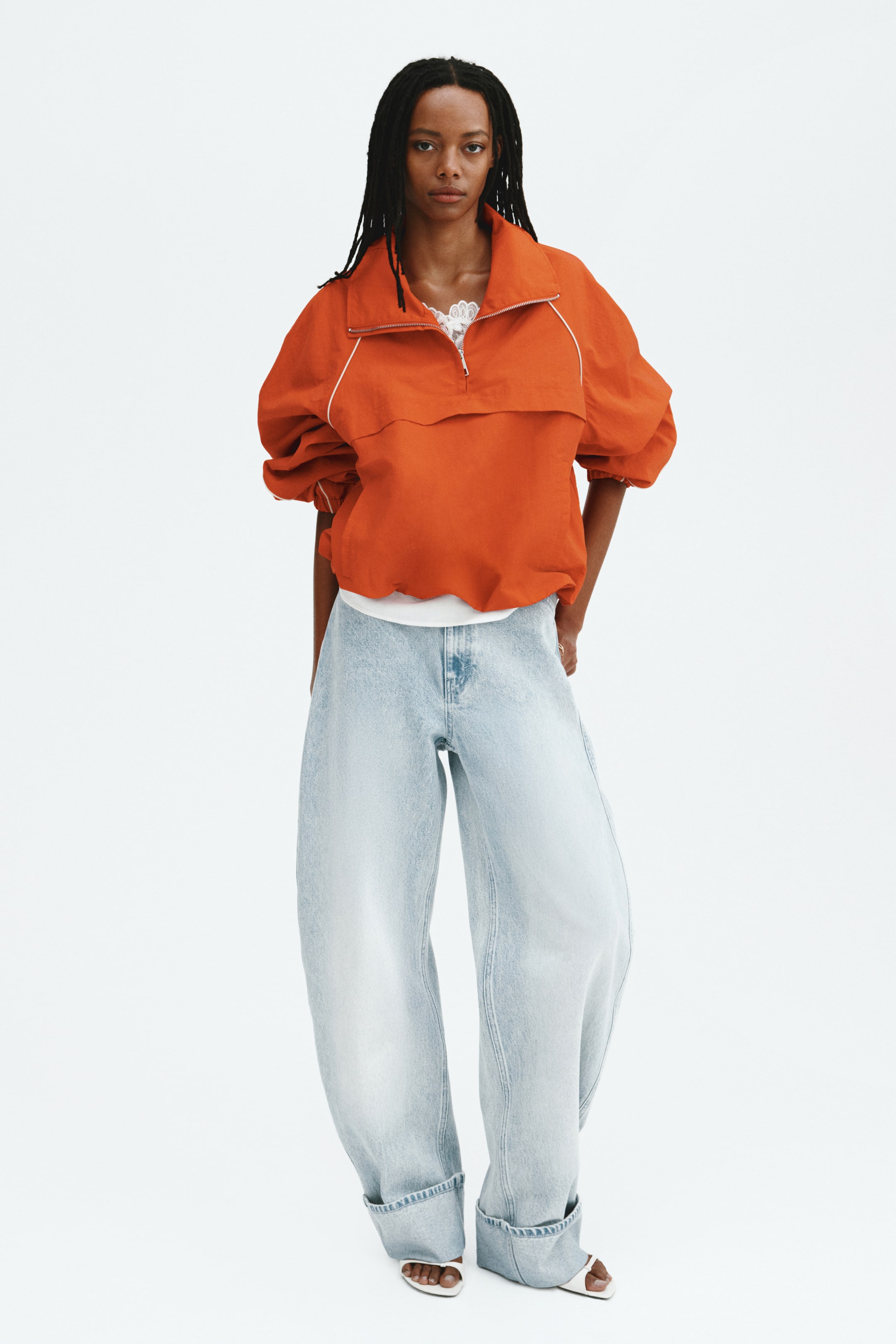 Größeres Bild anzeigen: Hellblaue Jeans im Used-Look werden vom Model getragen, mit normaler Taille und Knopfverschluss, Fronttaschen und einem voluminösen, geschwungenen Bein, das zu einem umgeschlagenen Saum verjüngt. Die Jeans treffen auf die Spitze weißer Sandalen mit offener Zehe, und ein weißes Oberteil wird geschichtet und in die Taille gesteckt.