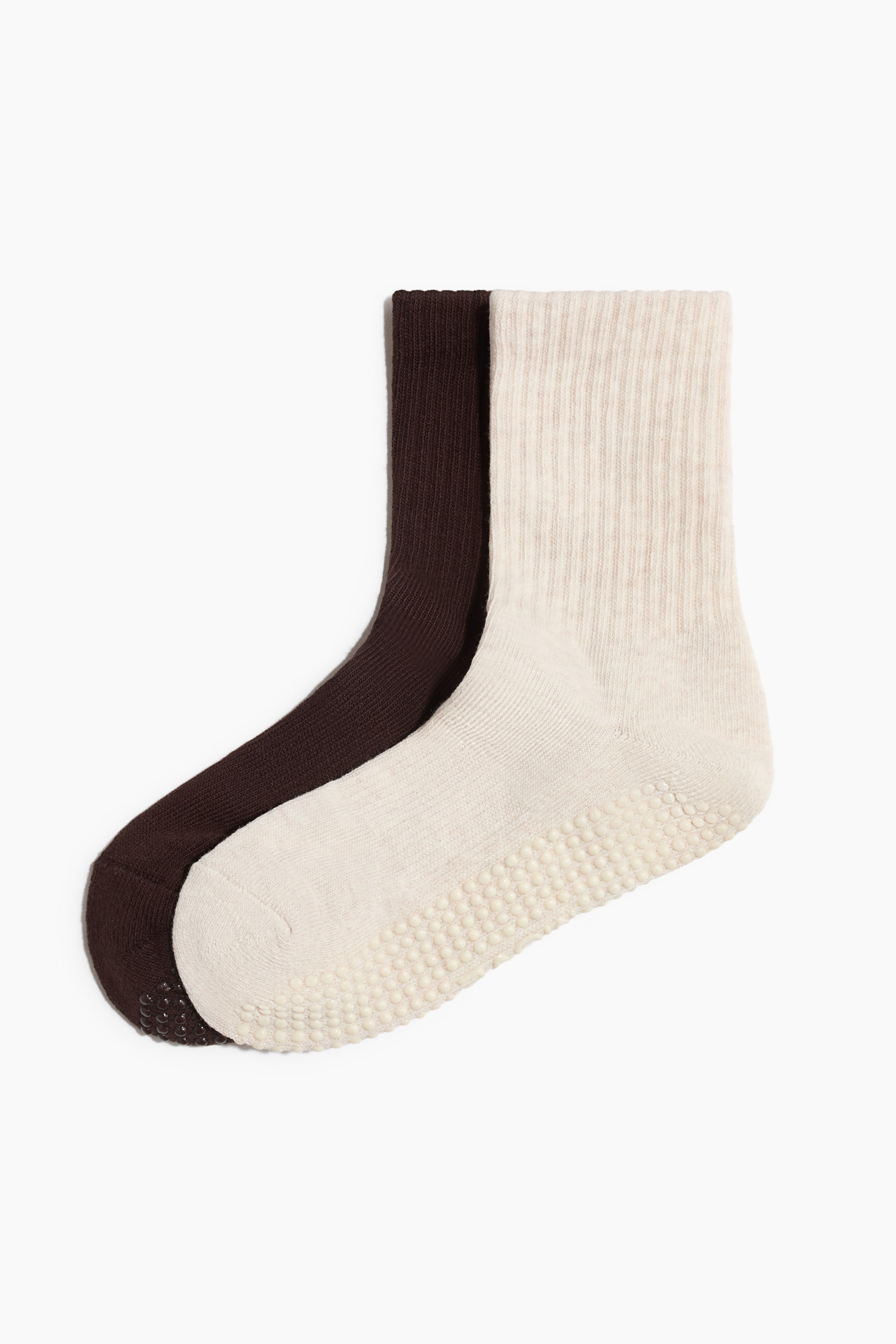 View larger image: An off-white sports sock is angled forward, revealing its sole with anti-slip protectors, while a dark brown sports sock is positioned behind it, also showing anti-slip protectors at the toe. Both socks are displaying ribbed shafts.
