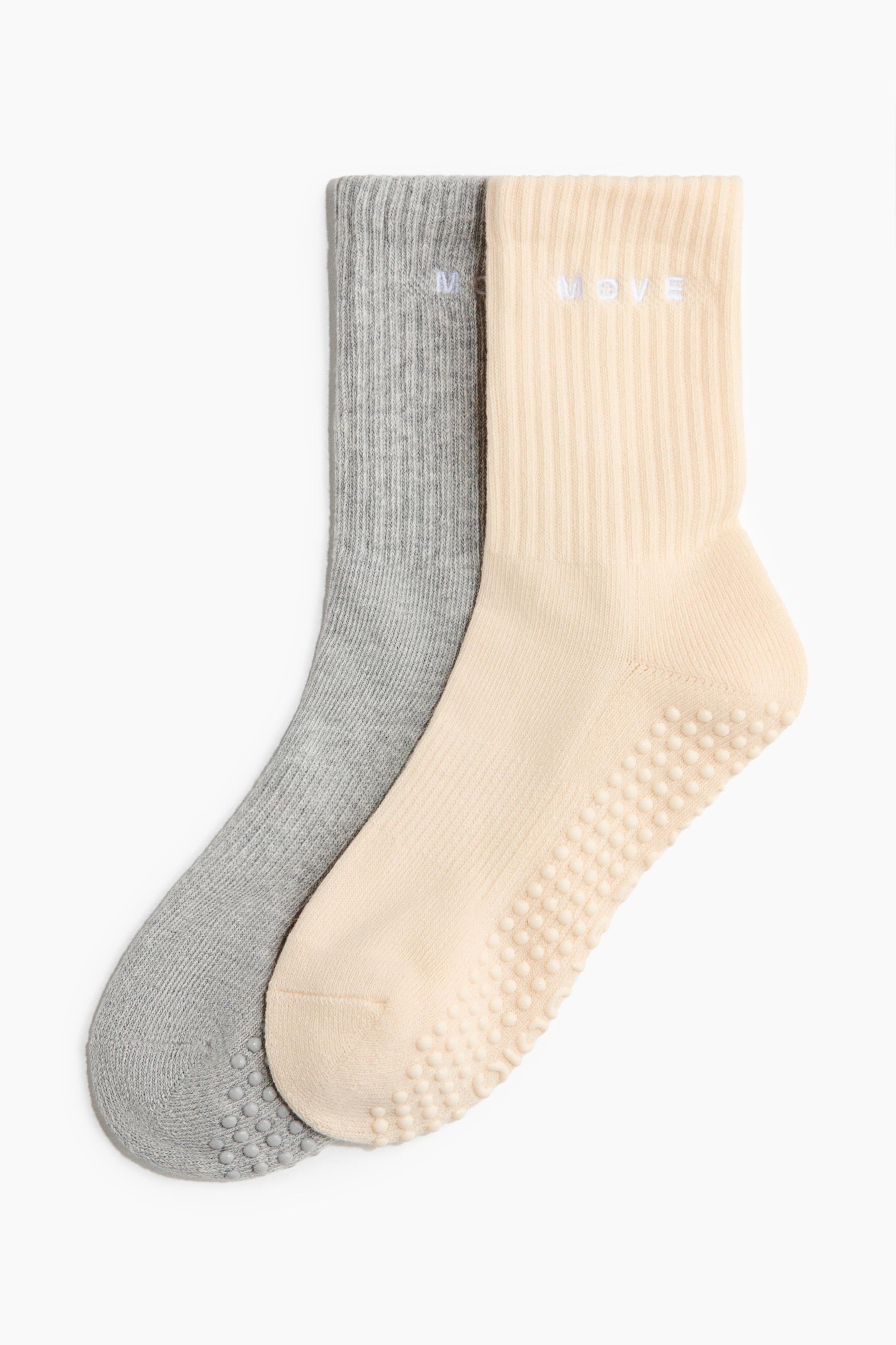 View larger image: Two fine-knit sports socks, one in light grey and one in light cream, are lying side-by-side, both featuring ribbed shafts with "MOVE" embroidered on the upper part and small, raised anti-slip dots on their soles.