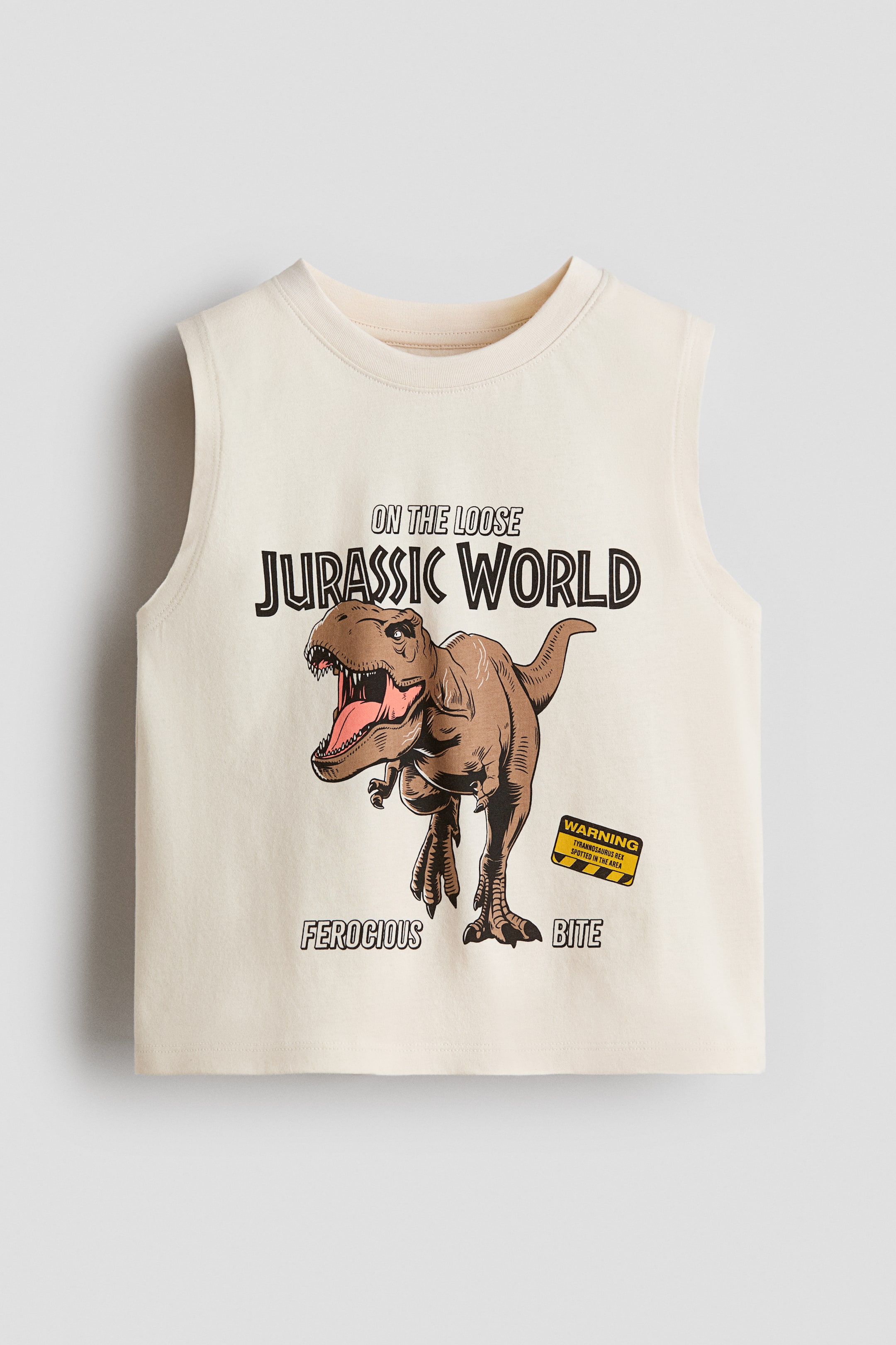 Voir une image plus grande: Le haut sans manches crème est orienté vers l'avant, avec un col rond et une coupe sans manches. Il affiche un grand graphique sur le devant, comprenant le texte audacieux "Jurassic World", un Tyrannosaurus Rex marron avec la bouche ouverte, un panneau "Attention" jaune et noir indiquant "Tyrannosaurus Rex repéré dans la région", et des phrases supplémentaires "En Liberté", "Féroce" et "Morsure".