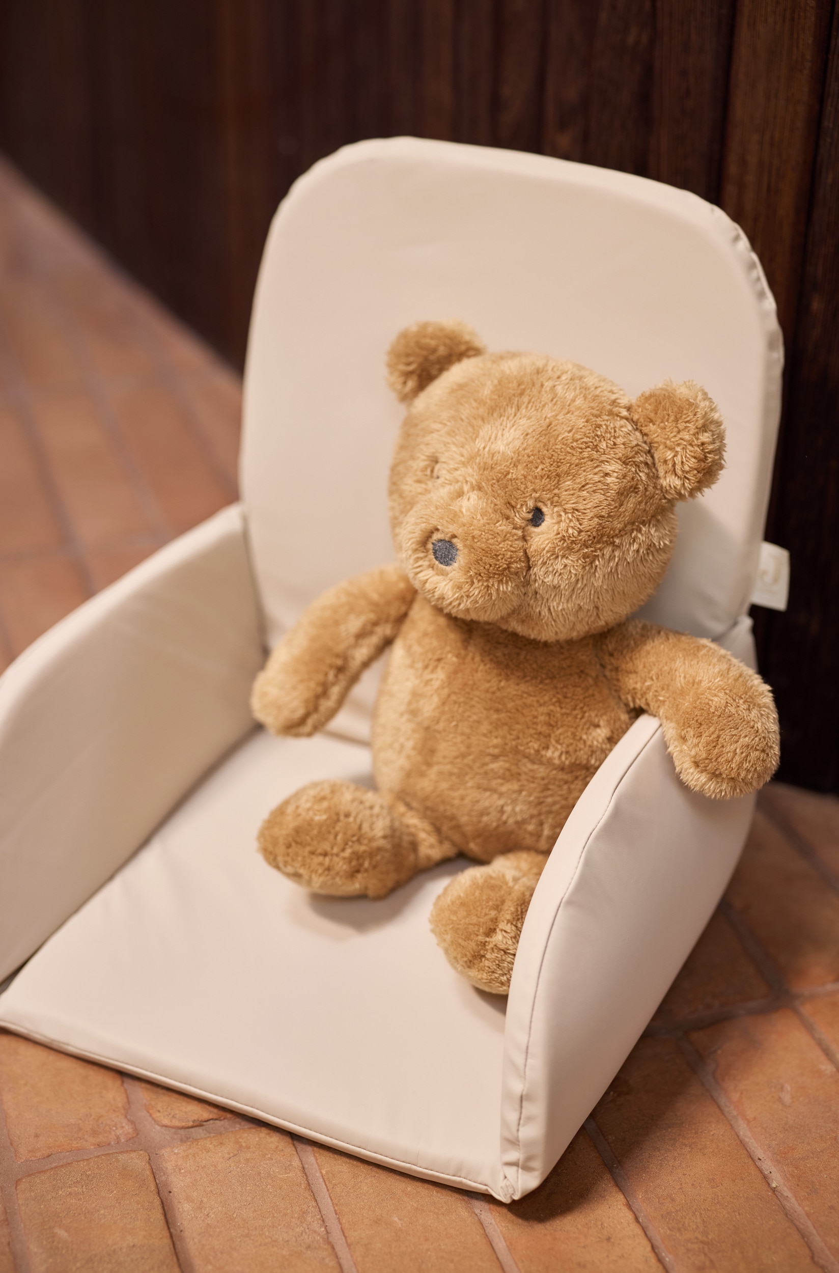 Un coussin dâinsertion beige pour chaise haute est prÃ©sentÃ© de face, avec un dossier rembourrÃ©, une assise plate et deux panneaux latÃ©raux de soutien incurvÃ©s. Le coussin est confectionnÃ© dans un tissu lisse et porte une petite Ã©tiquette de marque fixÃ©e sur le bord gauche du dossier.