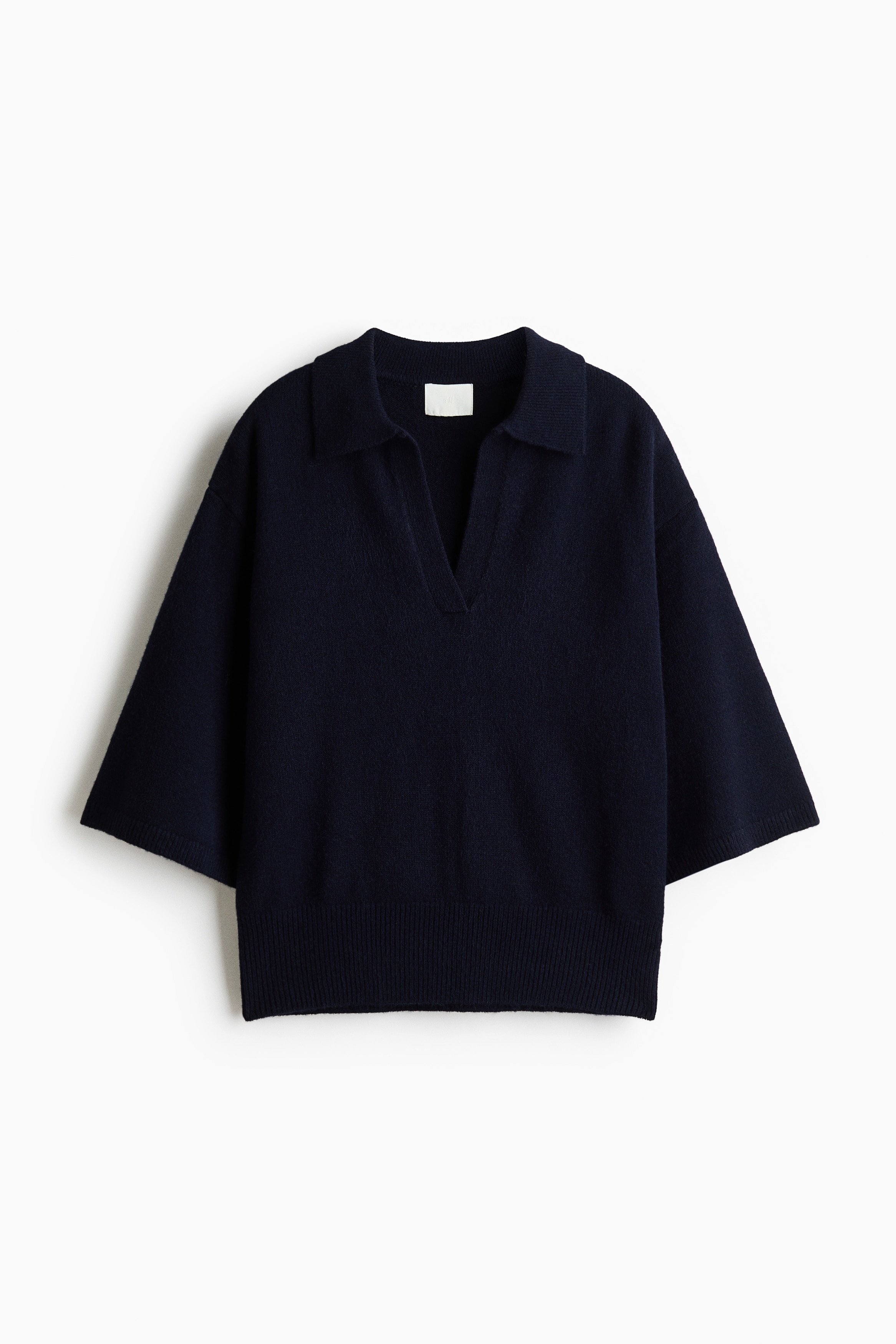 Un polo en tricot fin bleu marine foncÃ© est prÃ©sentÃ© de face, avec un col ouvert, des Ã©paules tombantes et des manches longueur coude avec poignets cÃ´telÃ©s. Le polo affiche un ourlet cÃ´telÃ© et est superposÃ© sur un T-shirt blanc qui dÃ©passe au niveau de lâencolure et de la taille.