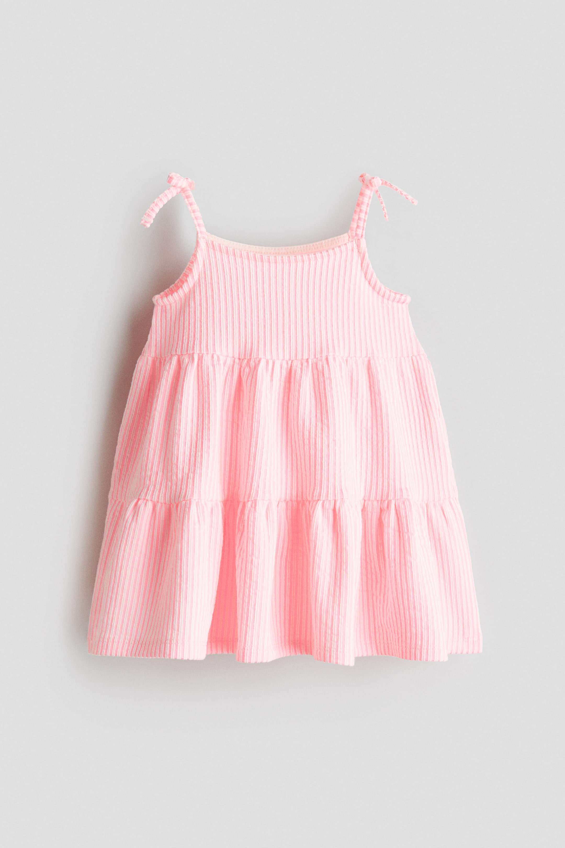 View larger image: The pink sleeveless empire-line dress showcases a soft, textured jersey with vertical ribbing visible from the front. It is crafted with narrow shoulder straps embellished with sewn-on bows at the top, and a tiered skirt gracefully flows from the empire waist.