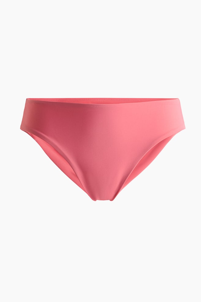 A coral pink bikini bottom is displaying a smooth, solid-colored fabric. It is featuring a wide waistband and a classic brief cut, appearing from a slightly downward, front-facing angle. - 1