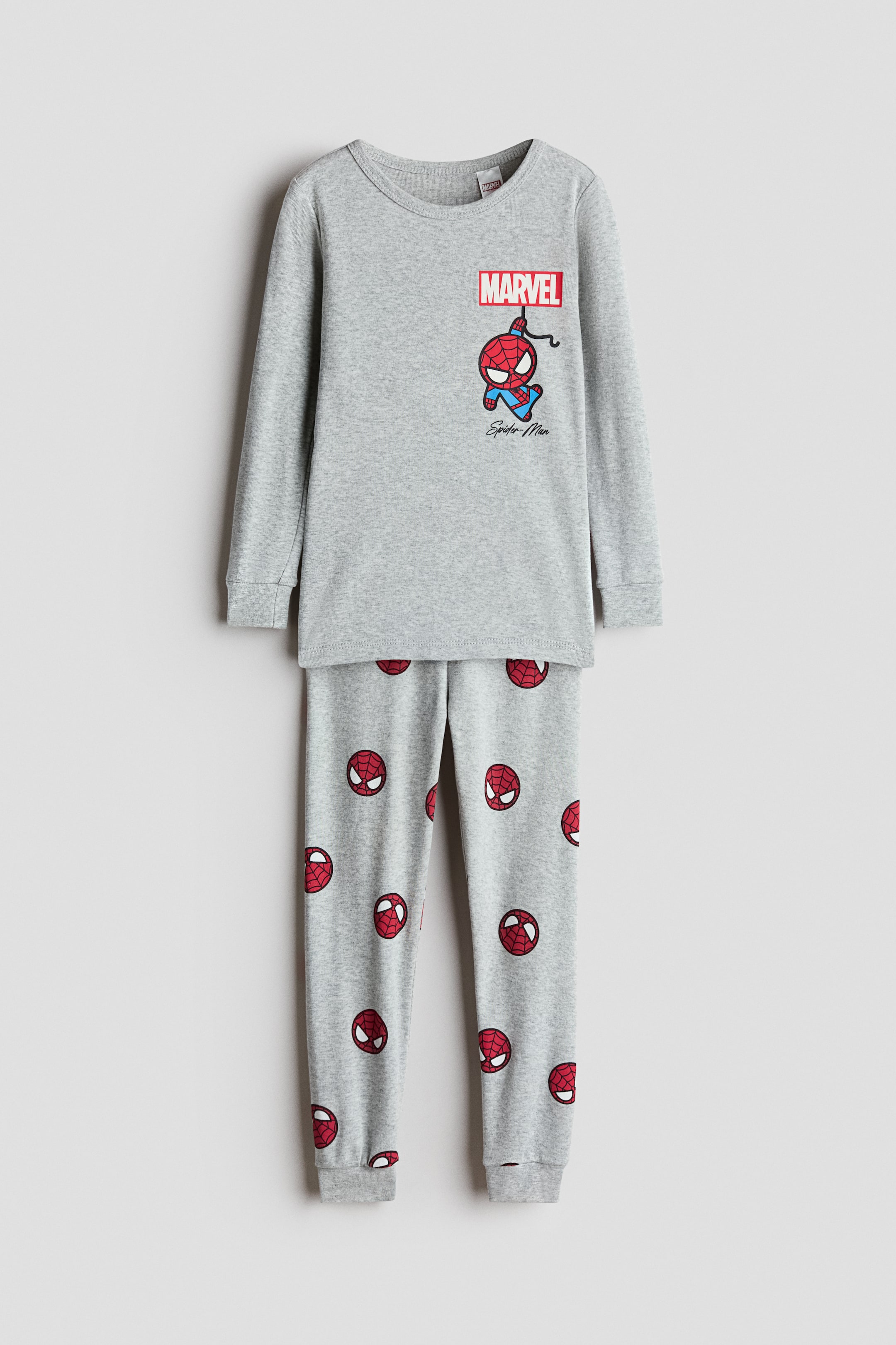 View larger image: A grey cotton jersey pyjama set is shown from the front, featuring a long-sleeved top with a round neckline, ribbed cuffs, and a chest graphic of Spider-Man hanging beneath a red "MARVEL" logo. The matching grey pants are decorated with an all-over print of Spider-Man masks and feature ribbed cuffed hems.