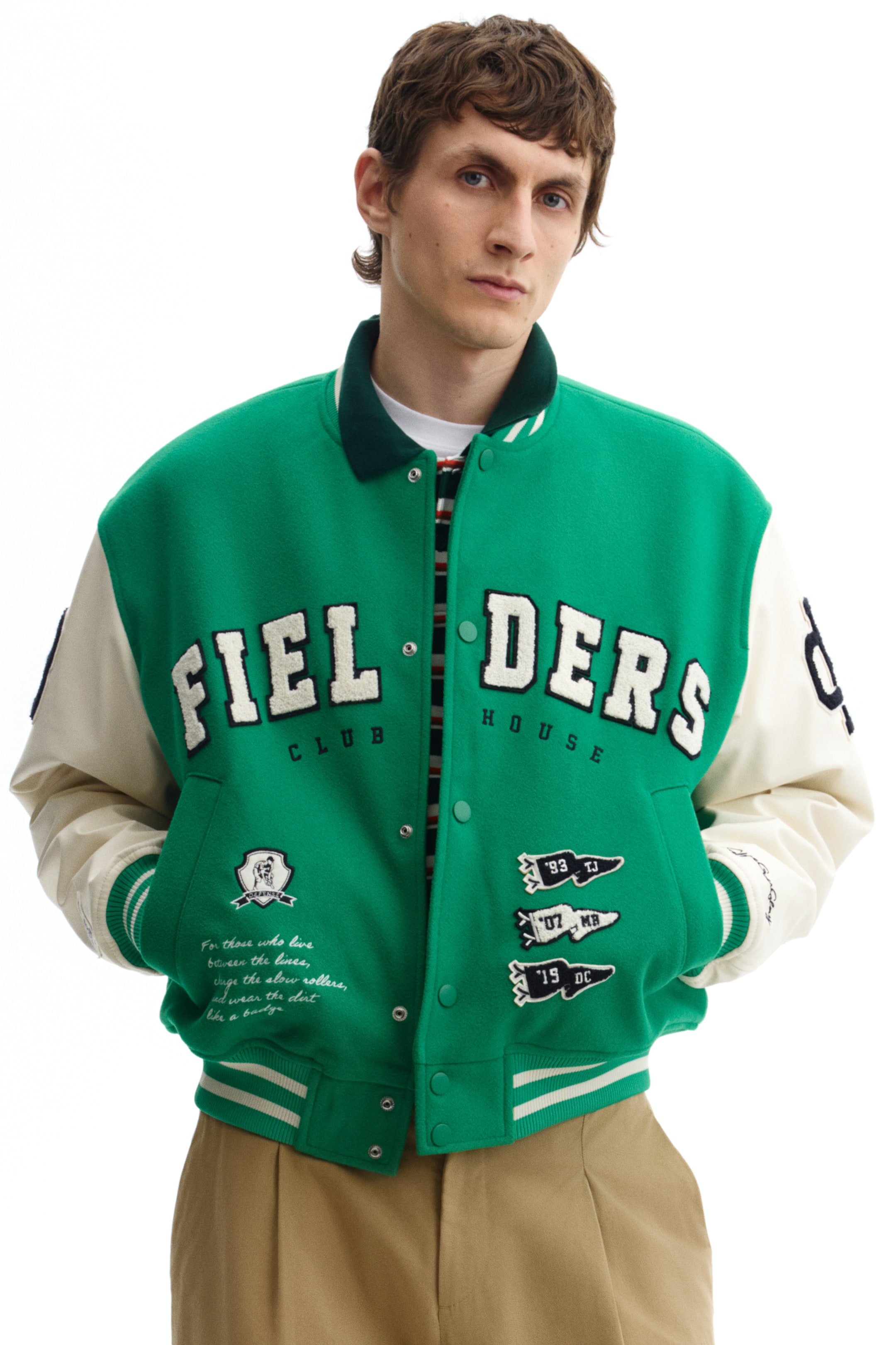 View larger image: A green-and-cream varsity jacket is shown from the front, featuring a dark green ribbed collar, snap-button closure, and striped ribbed cuffs and hem. White chenille lettering "FIEL DERS" appears across the chest, with "CLUB" and "HOUSE" below, accompanied by a crest patch, three pennant-shaped patches, and script text.