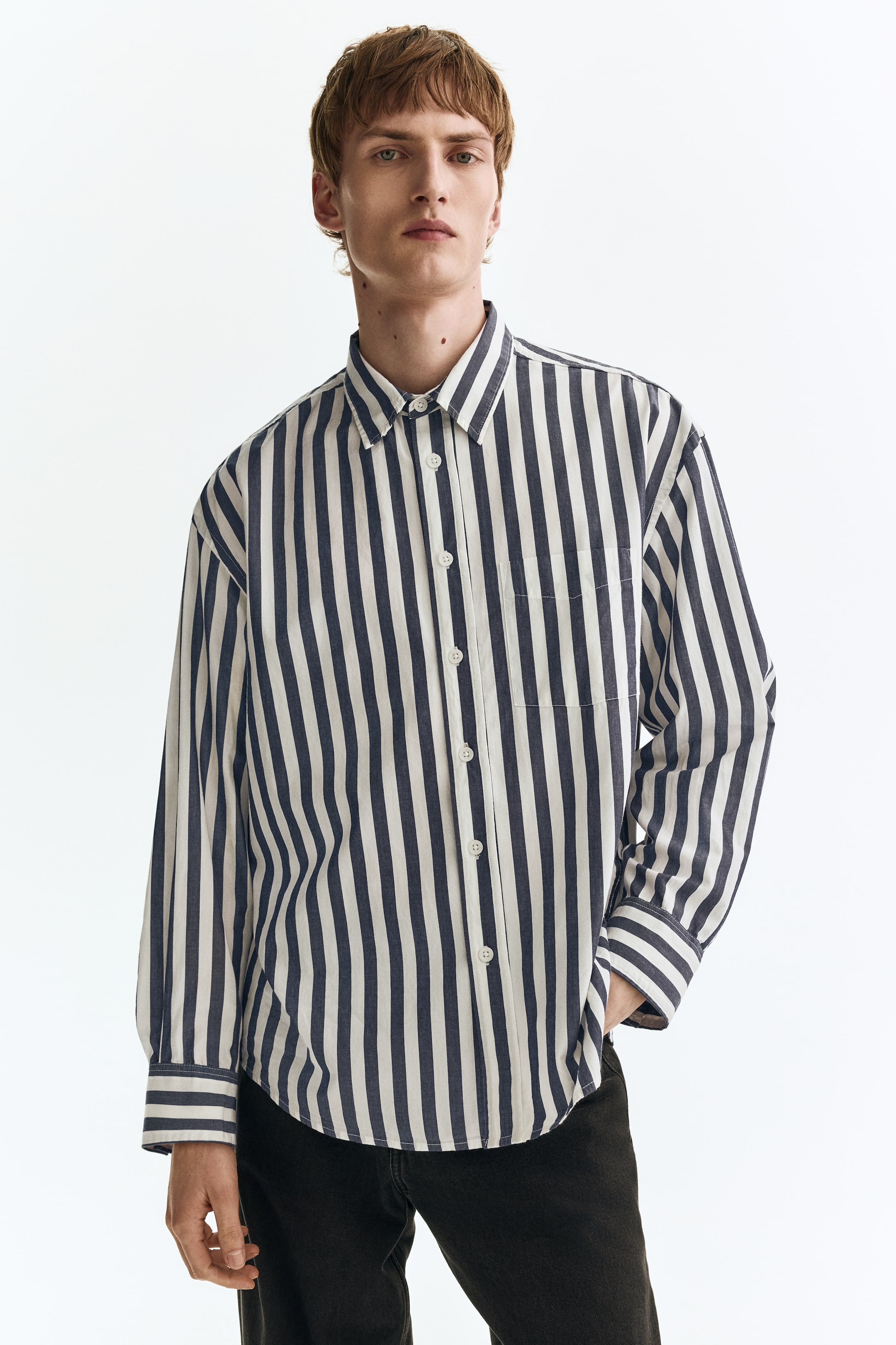 View larger image: A vertically striped shirt showcases navy blue and off-white stripes, a pointed collar, and a full button-front placket with white buttons. It also features a single patch pocket on the left chest, long sleeves with buttoned cuffs, and a curved hem, offering a relaxed fit from a forward-facing angle.