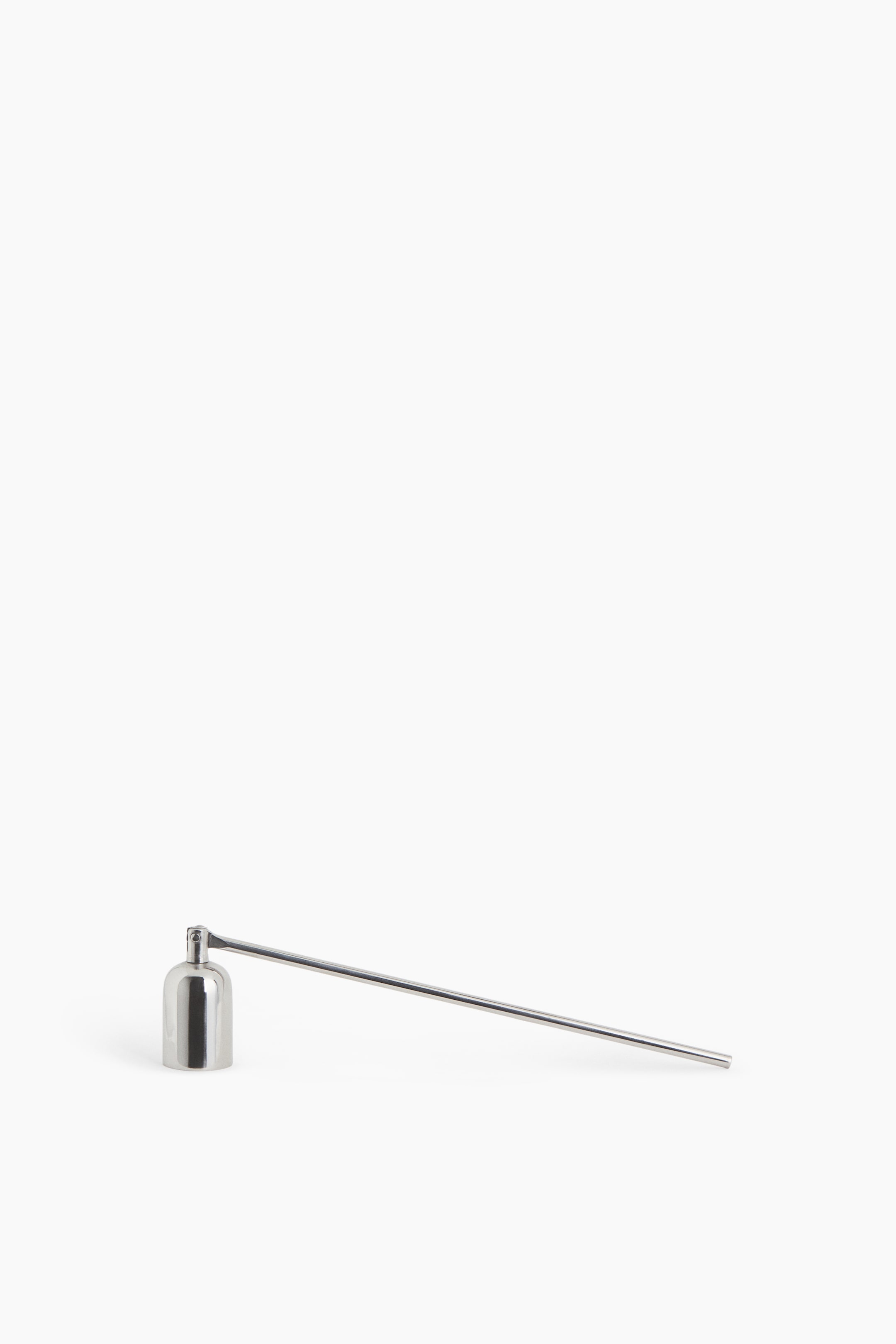 View larger image: A polished silver metal candle snuffer is resting, featuring a small, cylindrical bell cap connected by a hinge to a long, slender handle. The bell cap is standing upright while the handle is extending diagonally to the right.