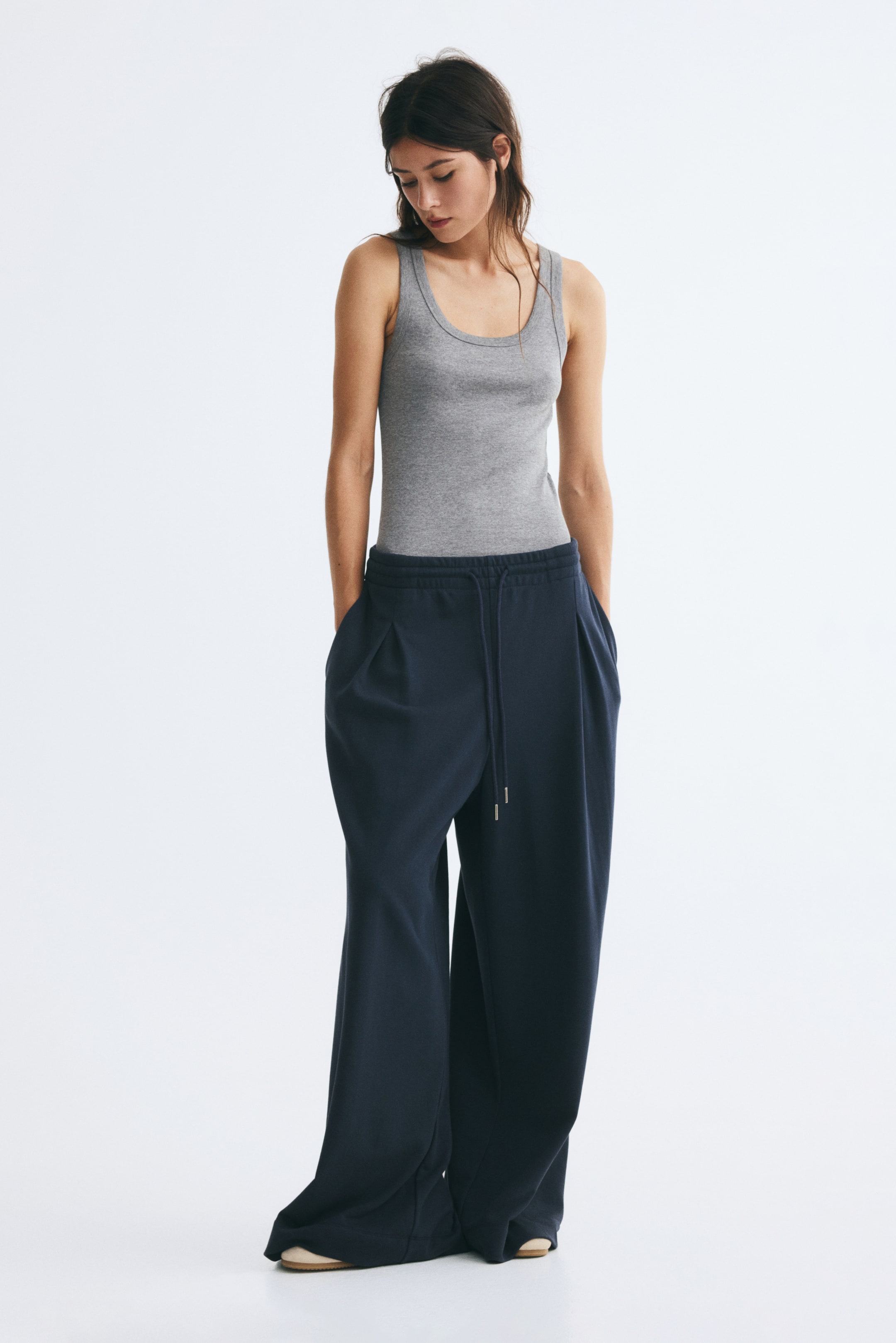 View larger image: The model is wearing a fitted grey tank top in ribbed cotton jersey, tucked into wide-leg dark blue drawstring trousers. The sleeveless tank top features a classic scoop neck and a form-fitting silhouette.