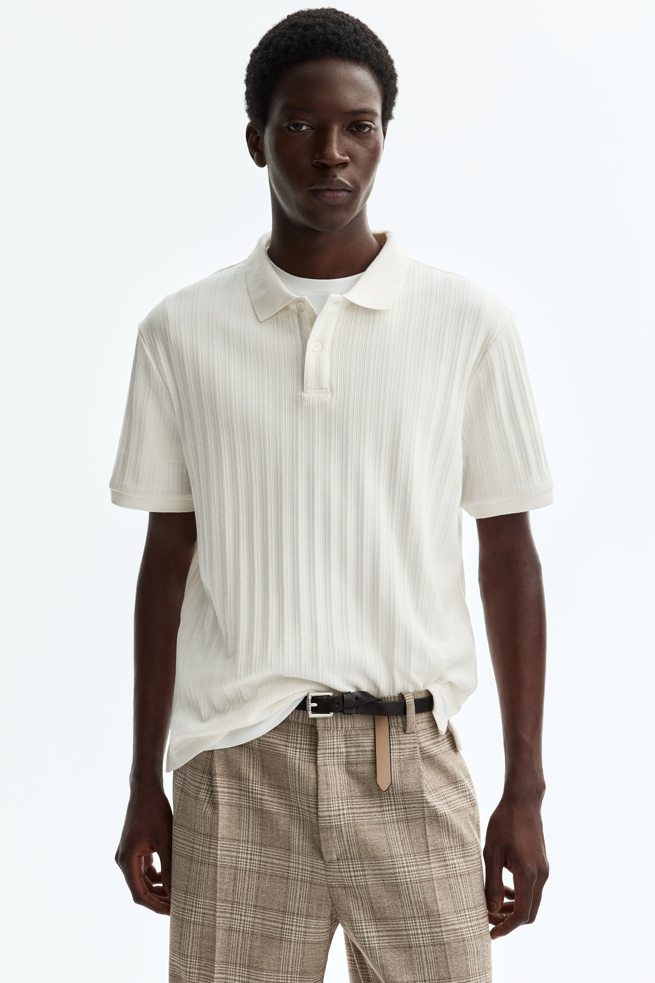 View larger image: A cream-coloured polo shirt is facing forward, displaying a vertical ribbed texture. It features a classic collar, a two-button placket, and short sleeves, with a white undershirt visible beneath.